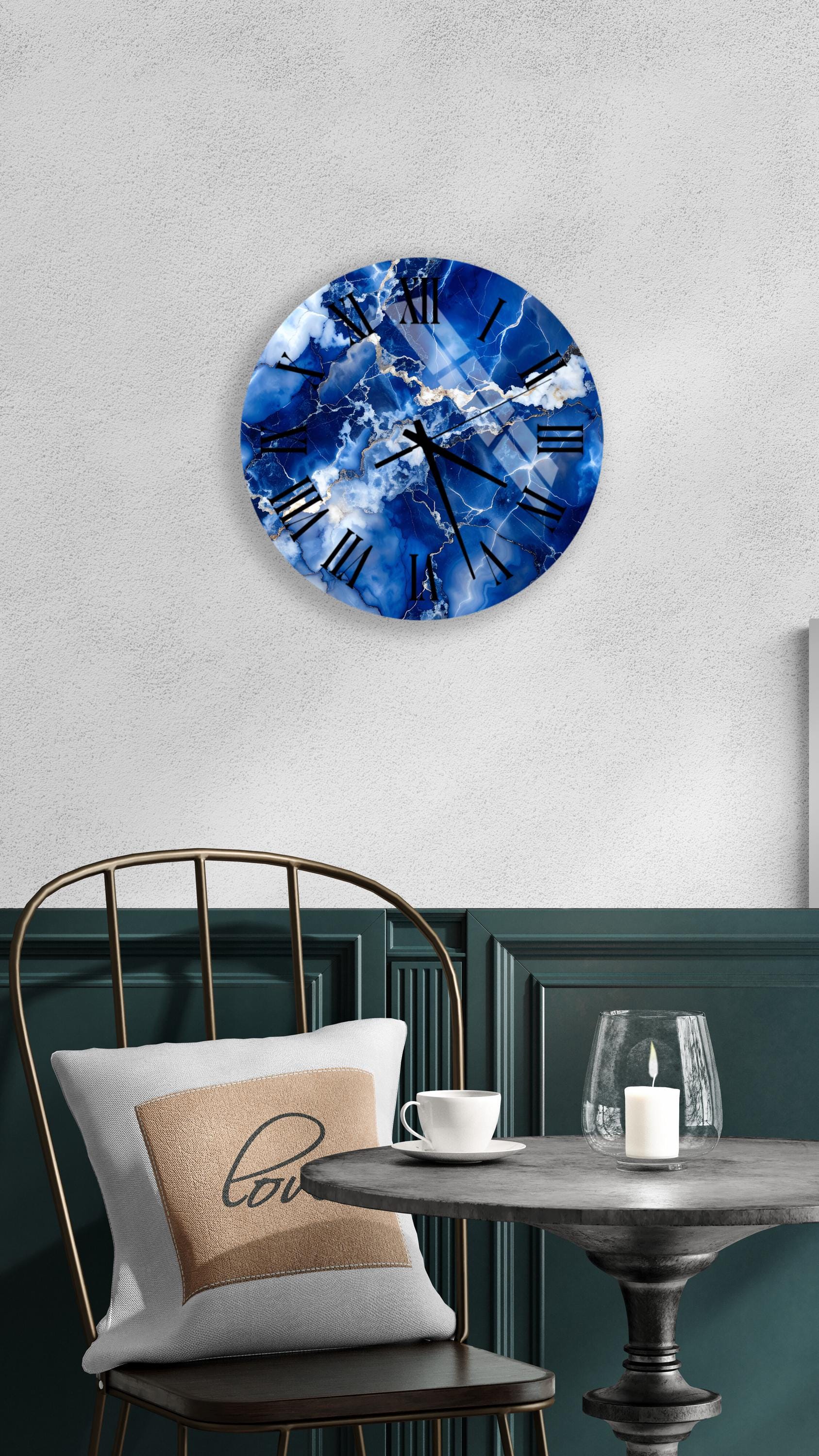 a wall clock with a blue marble design, mounted on a white wall above a dining table with a white tablecloth. The table is set with a white cup and a candle, creating a cozy and inviting atmosphere.