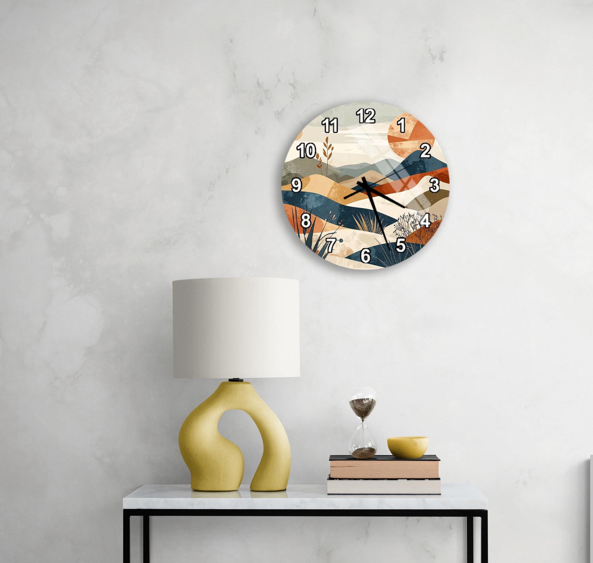 a modern clock with a colorful design hanging on a wall above a white table with a yellow lamp and a stack of books.