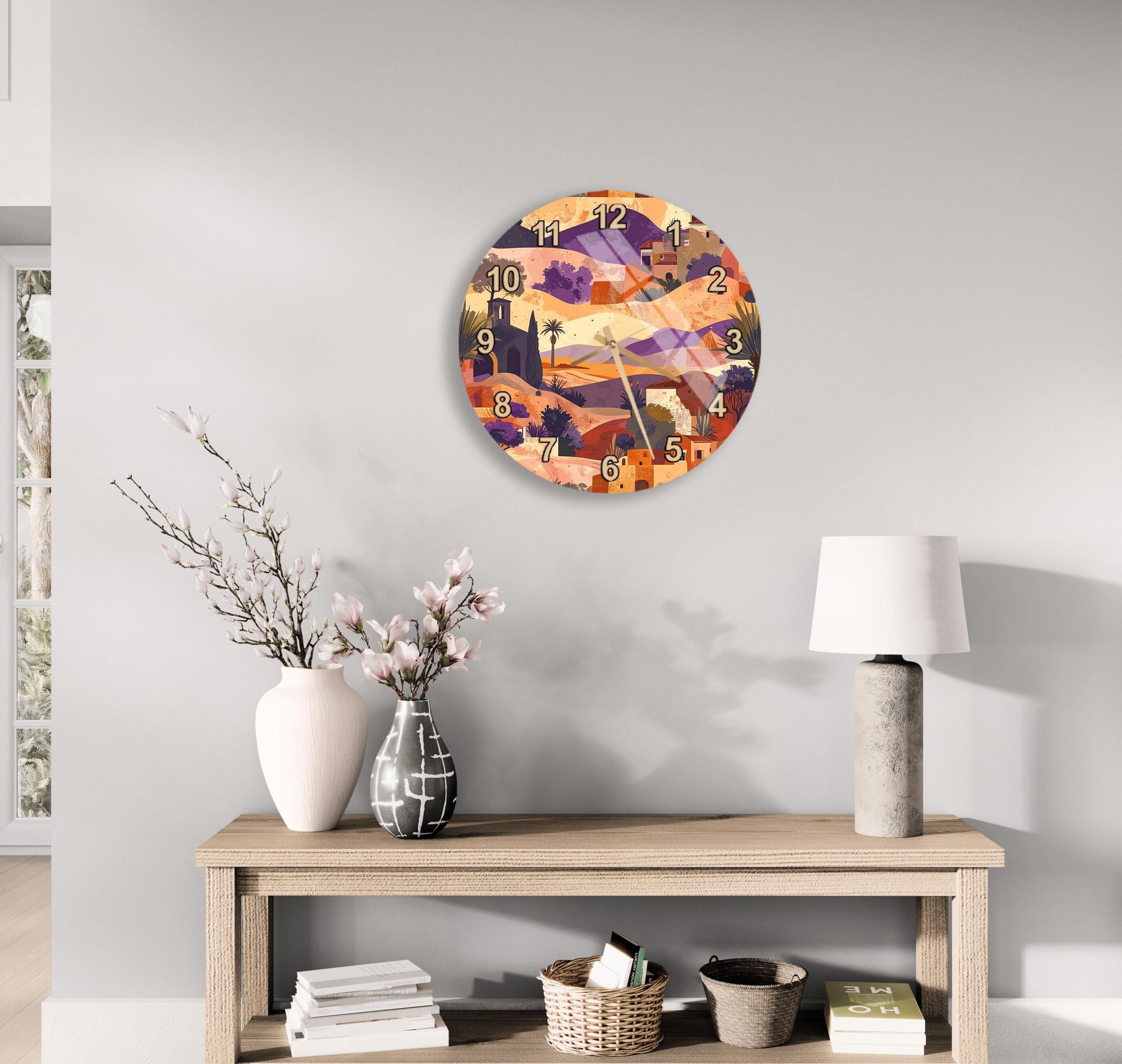 a wall clock with a colorful, abstract design hanging on a wall above a wooden table with various decorative items, including a vase with flowers, a lamp, and a stack of books.
