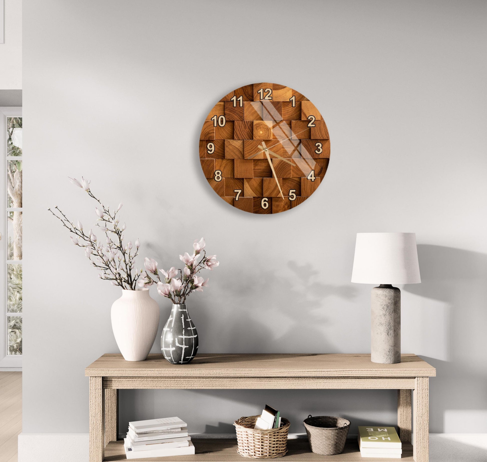 a wooden clock with a unique design hanging on a wall above a wooden table with various decorative items, including a vase with flowers, a lamp, and a stack of books.