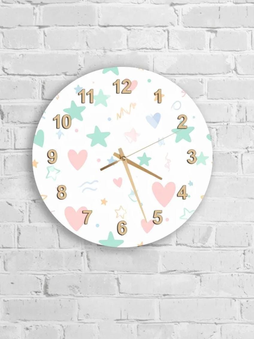 A round wall clock with a white background and colorful numbers and shapes, such as stars, hearts, and waves, is mounted on a white brick wall.
