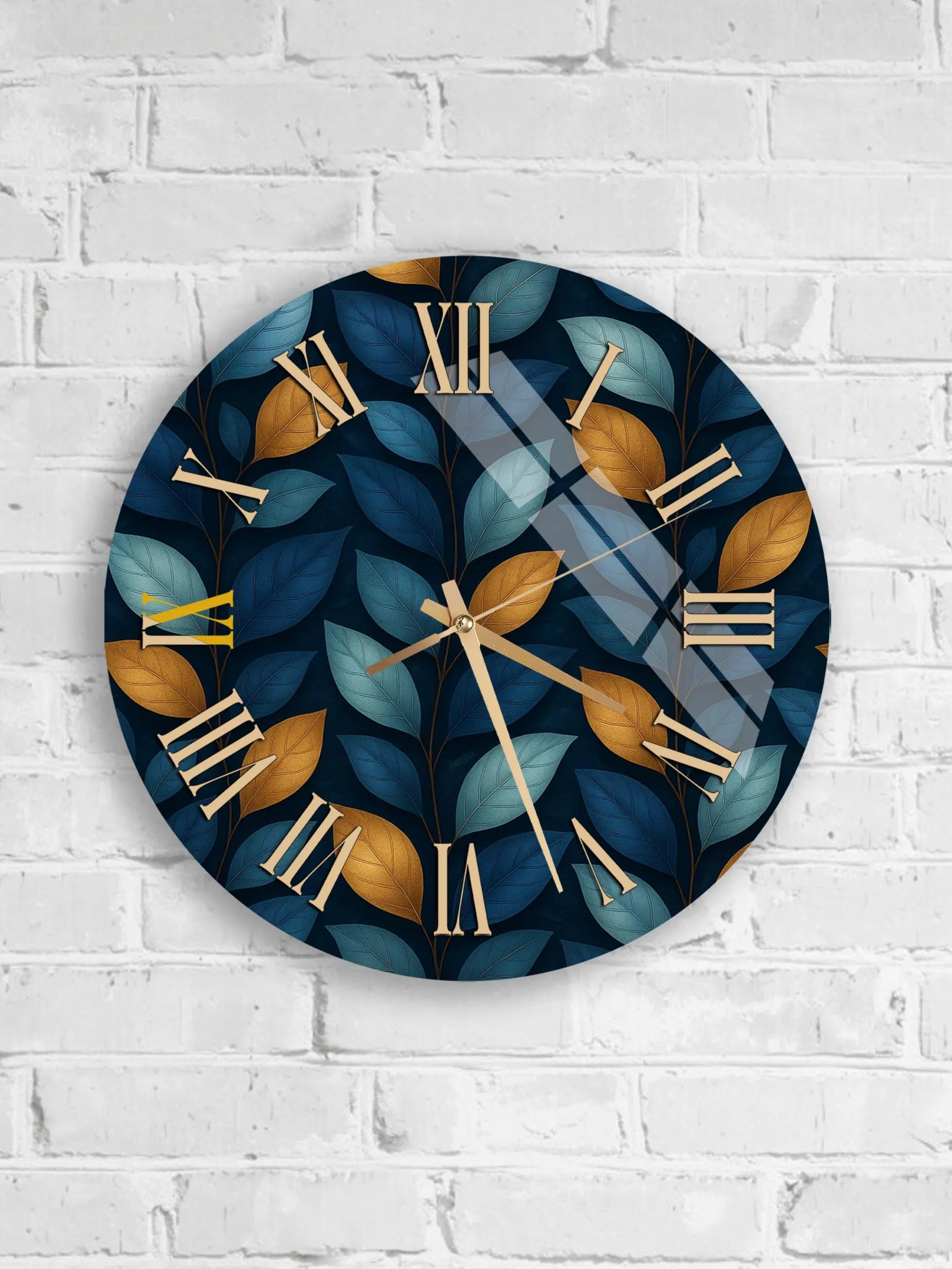 A round wall clock with a leafy leaf pattern and gold Roman numerals is mounted on a white brick wall.
