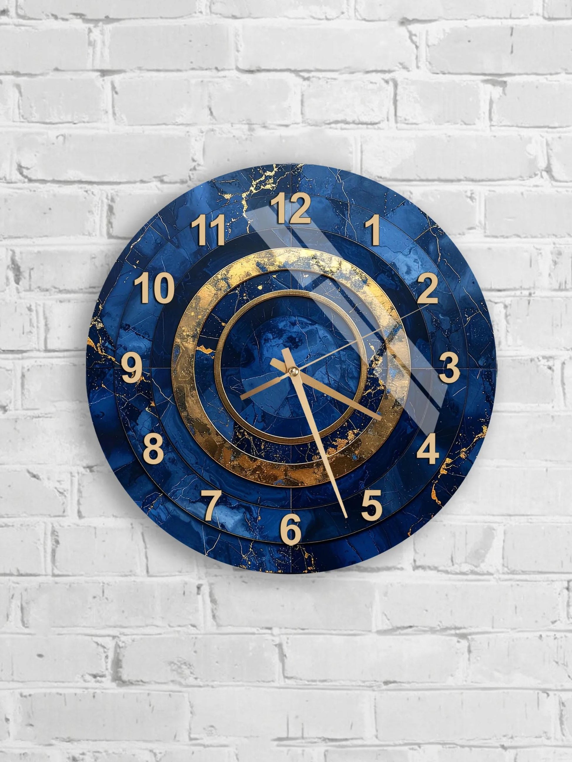 A blue and gold wall clock with a marble-like texture and gold hands is mounted on a white brick wall.