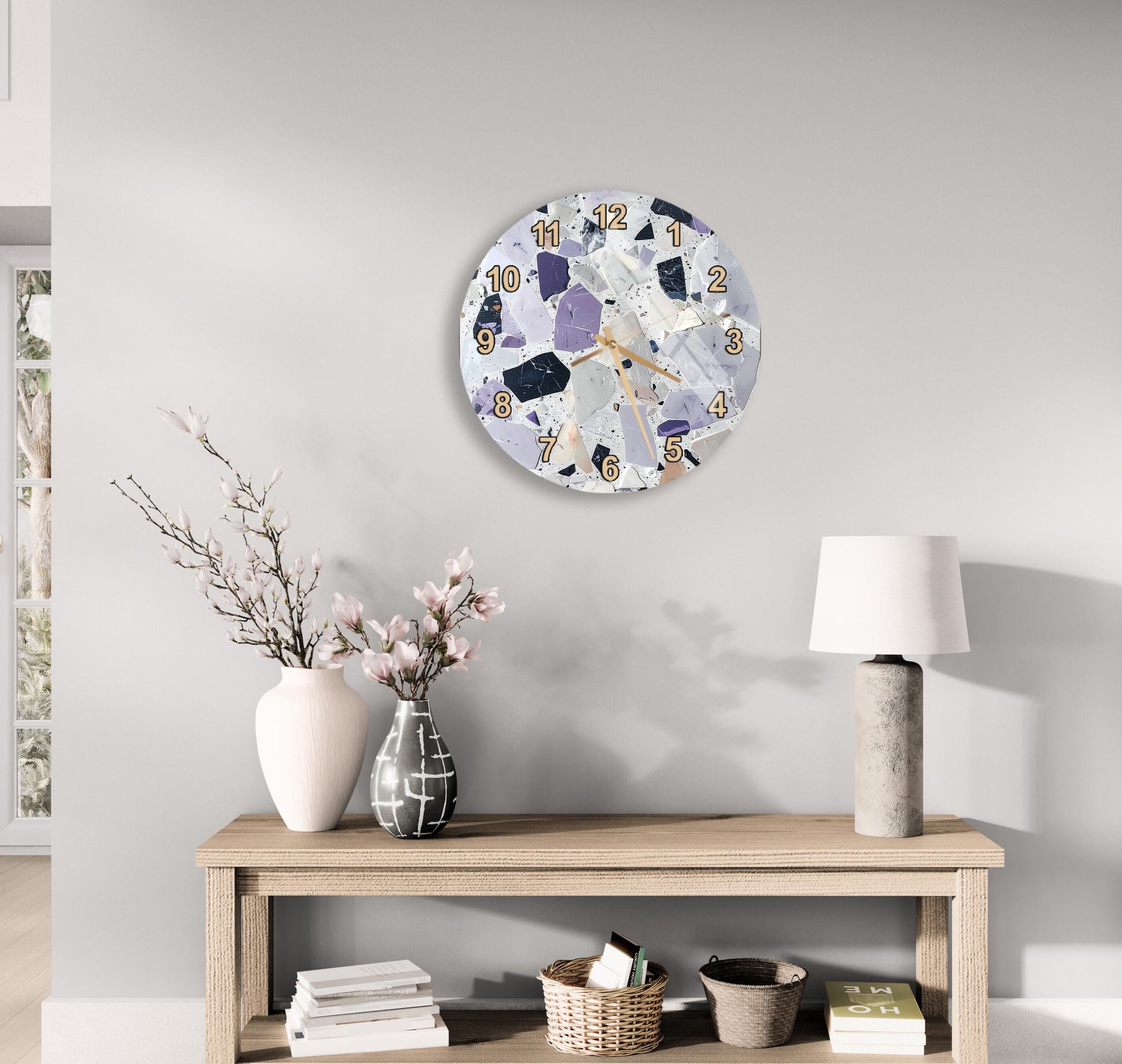 a modern and minimalist living room with a round clock on the wall, a wooden table with a lamp, a vase with flowers, and a stack of books.