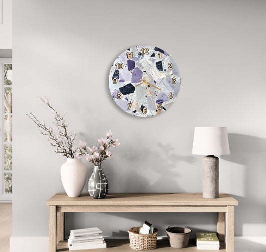 a modern and minimalist living room with a round clock on the wall, a wooden table with a lamp, a vase with flowers, and a stack of books.