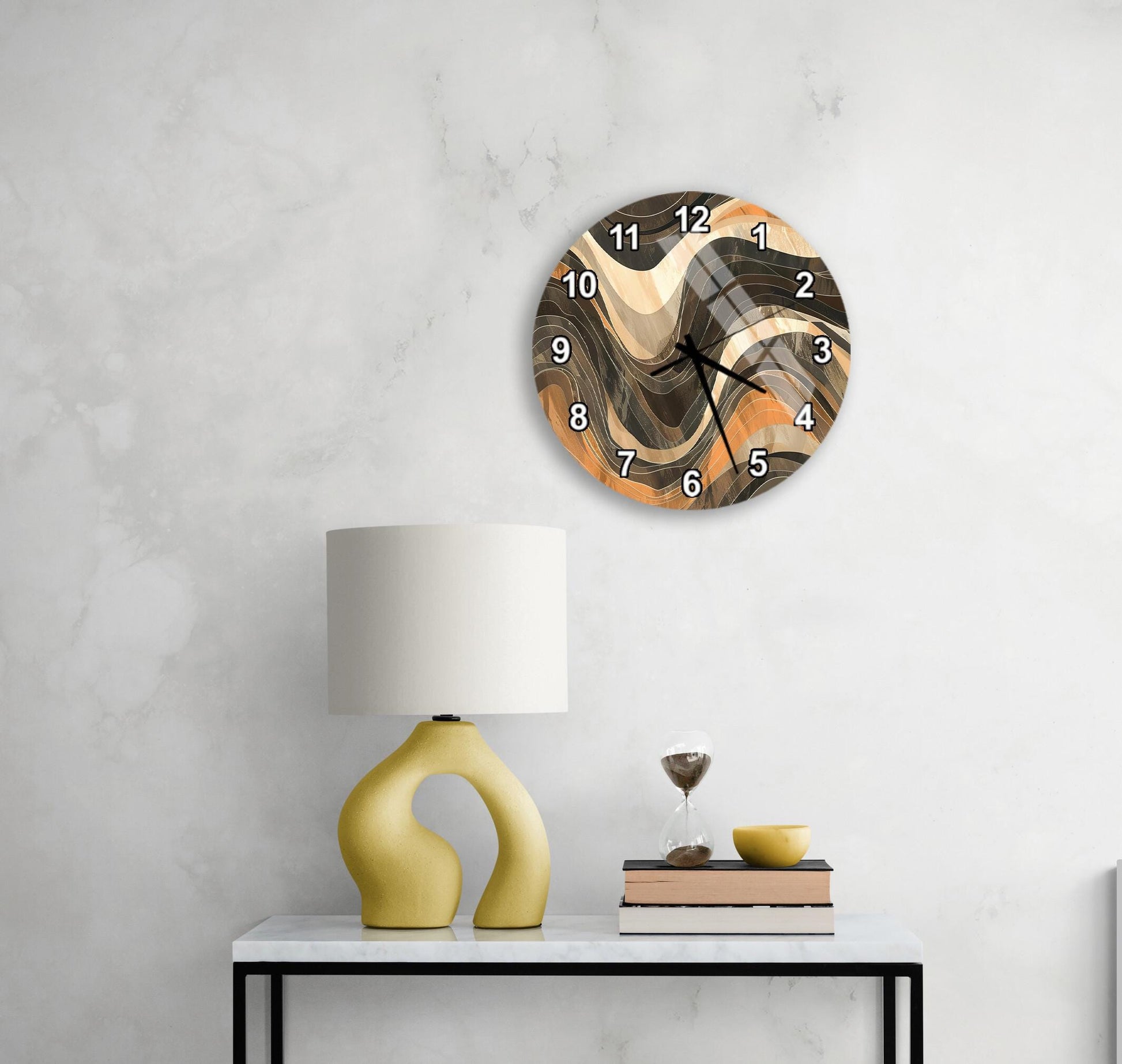a modern wall clock with a unique, abstract design, mounted on a wall above a white table with a yellow lamp and a stack of books.