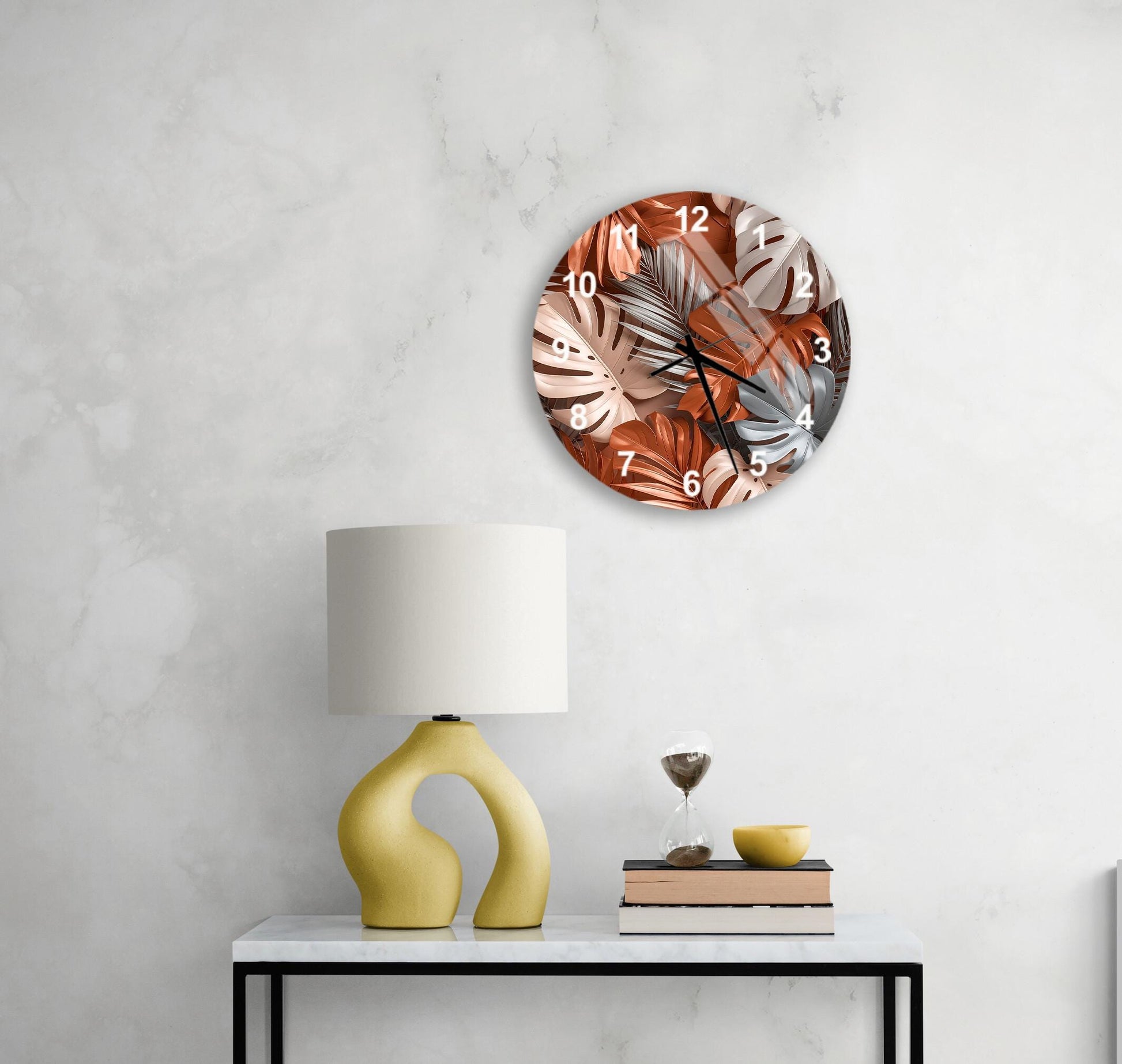 a modern living room with a round wall clock displaying a tropical leaf pattern, a yellow lamp with a unique curved base, a small table with a bowl and a book, and a white marble wall.