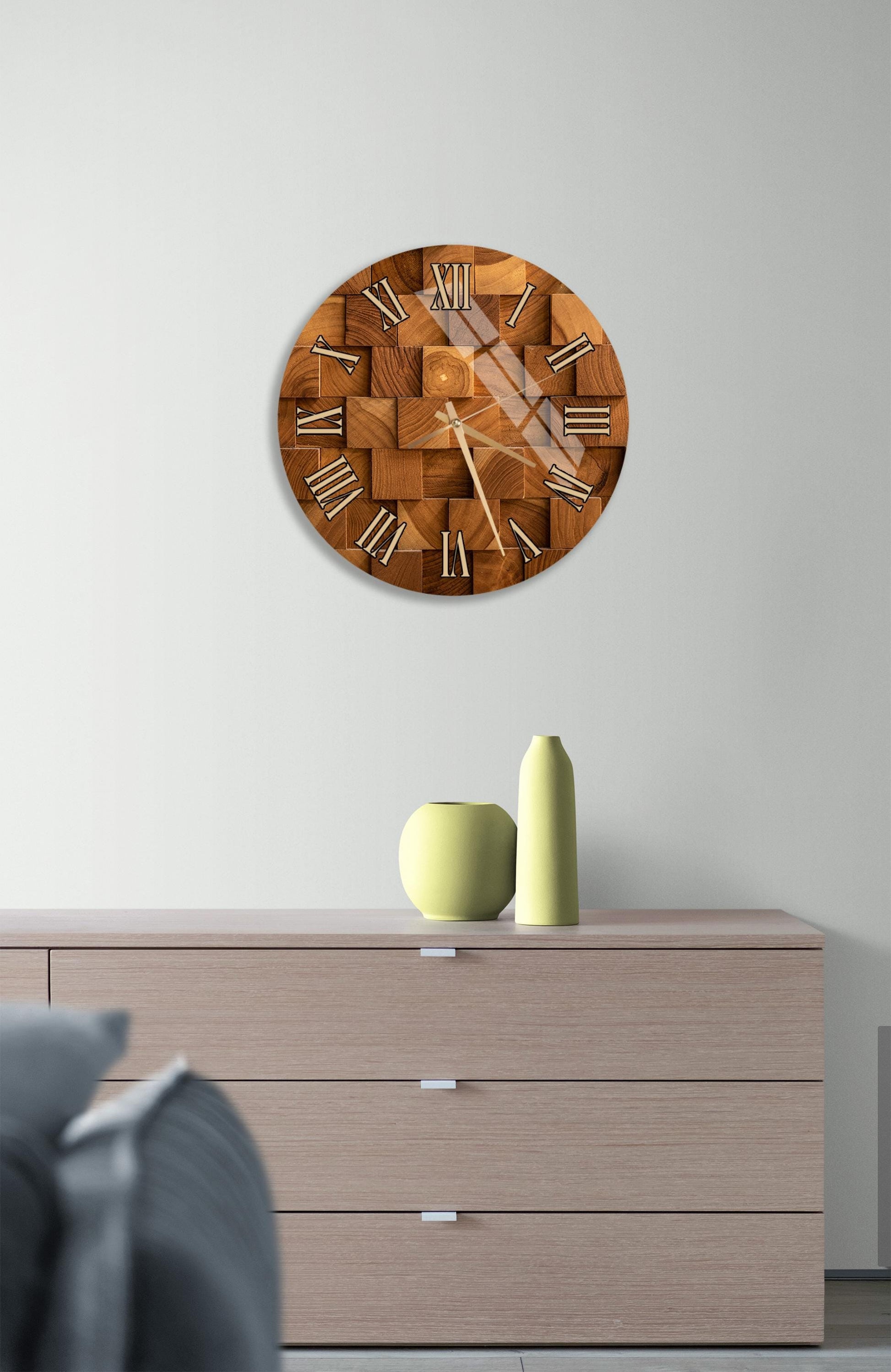 a wooden clock with Roman numerals mounted on a wall above a wooden dresser with three drawers.