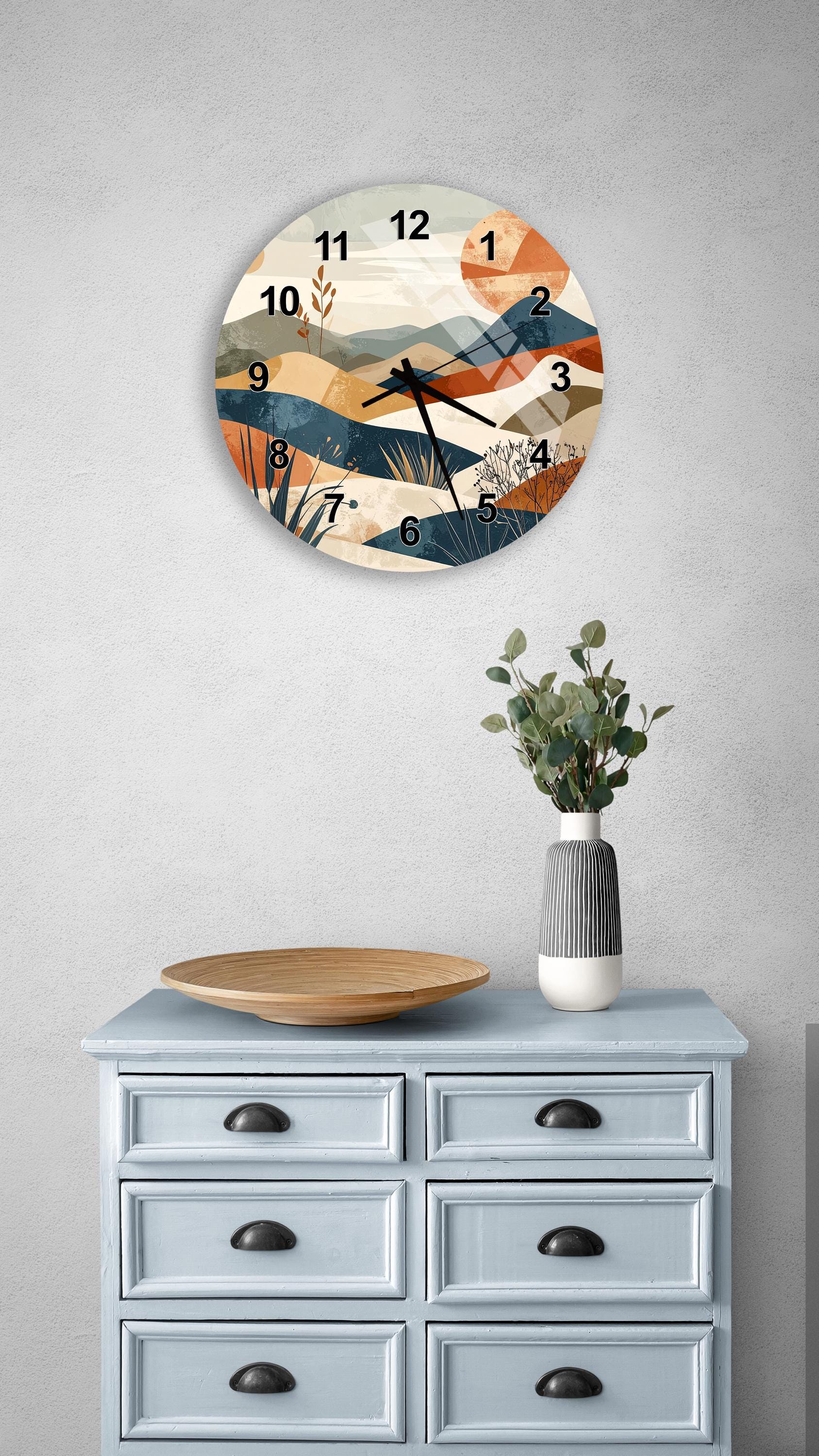 a wall clock with a landscape design, a wooden bowl on a light blue dresser, and a vase with greenery on a gray wall.