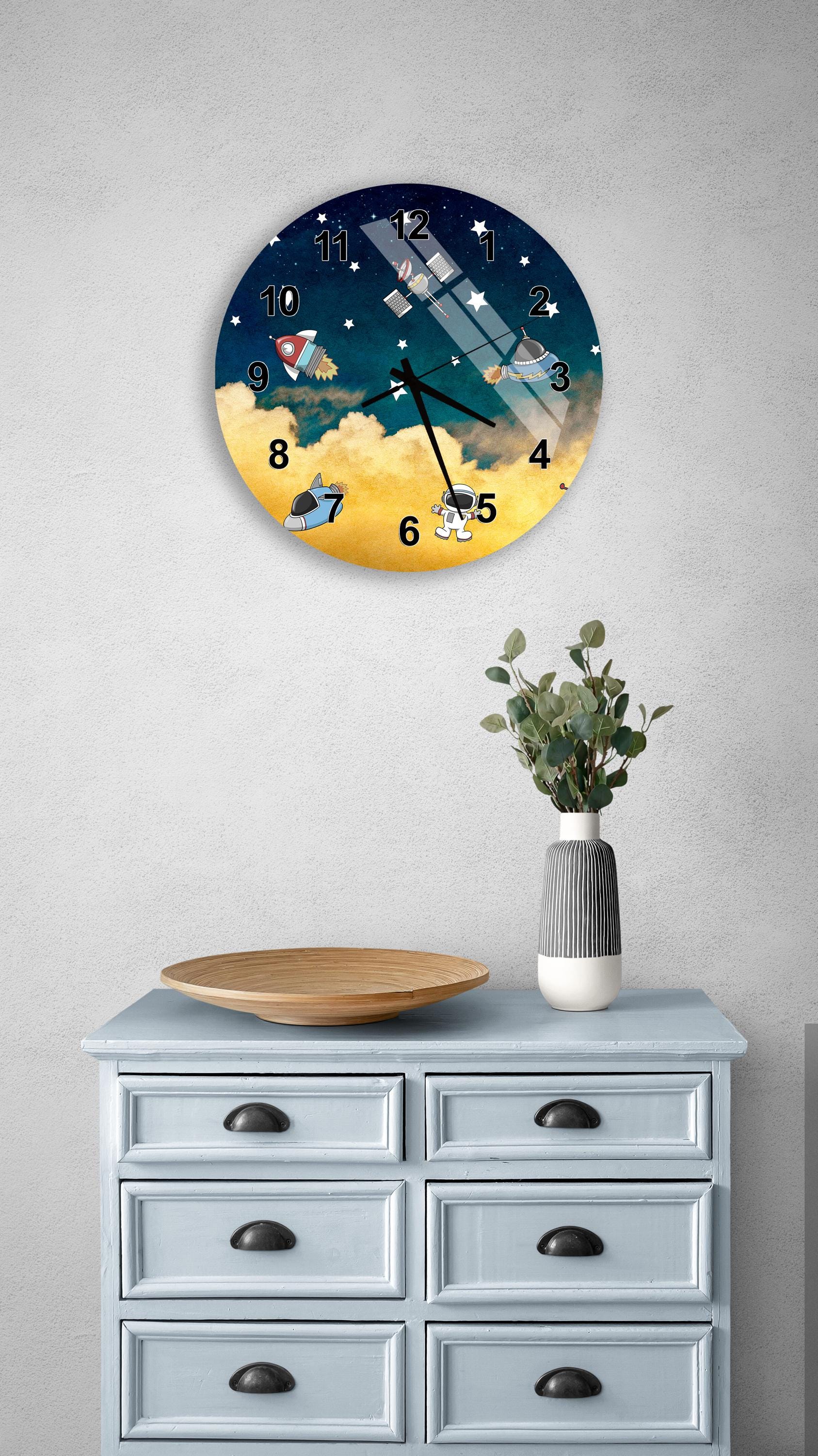 a clock with a space-themed design, mounted on a wall above a wooden dresser with drawers.