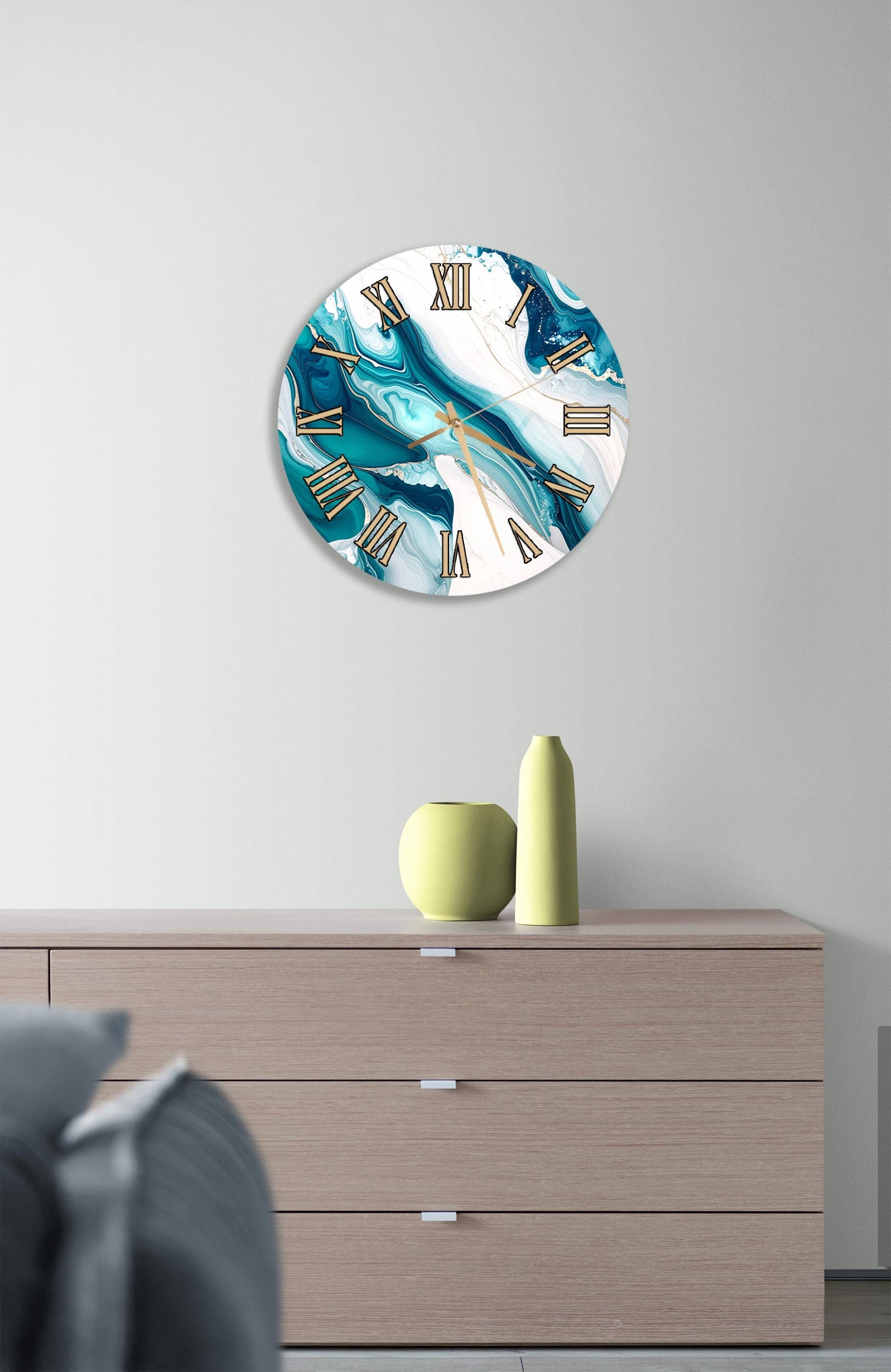 a wall clock with a marble-like design, mounted on a wall above a wooden dresser with three drawers. The dresser also has a small vase and a yellow pot on it.