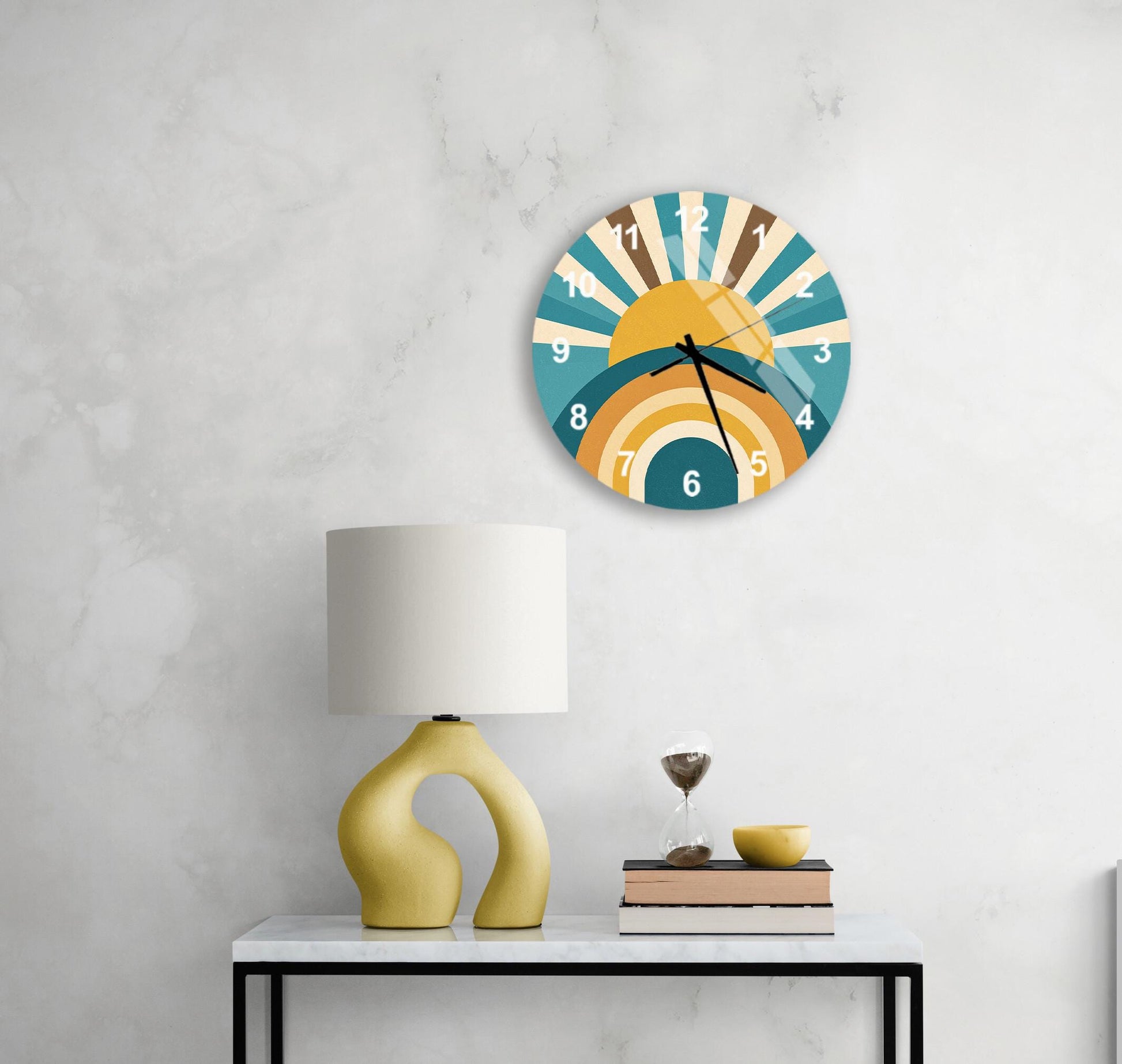 a modern wall clock with a sunburst design, a yellow lamp, a stack of books, and a glass of water on a white table.