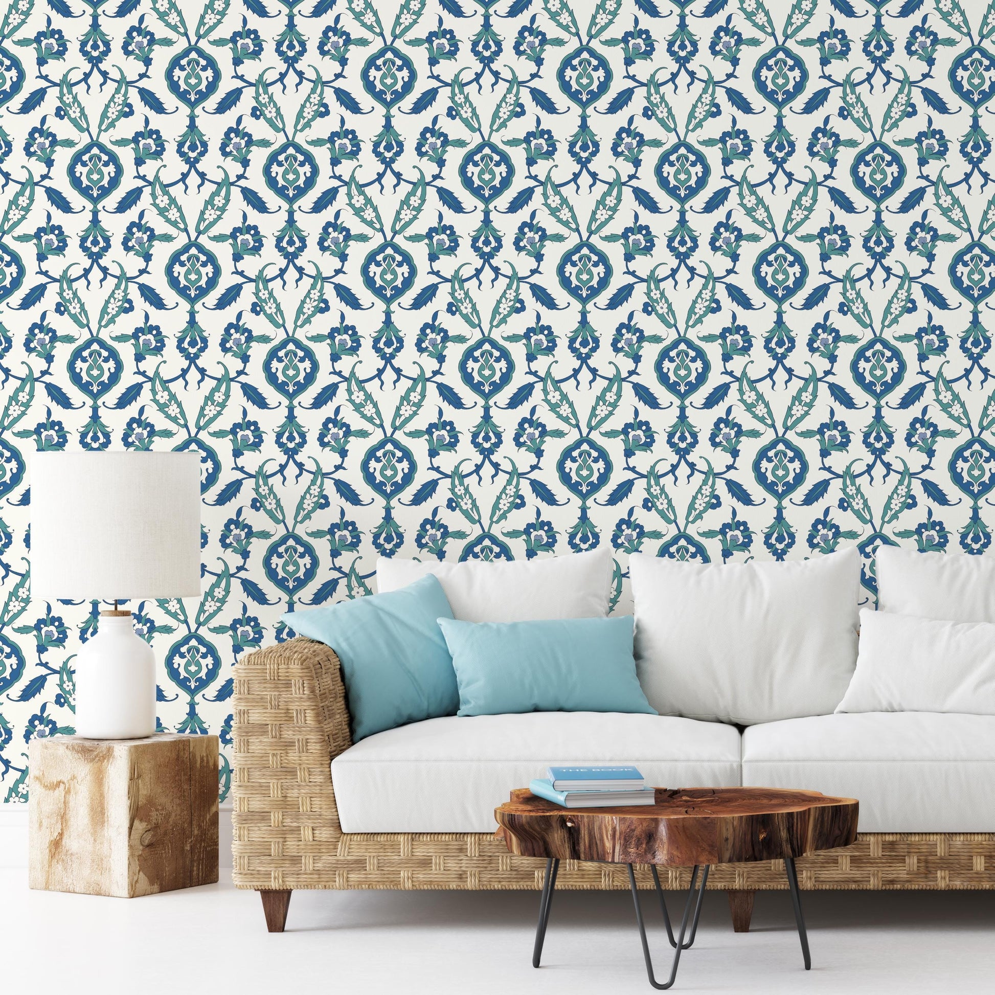 a living room with a white sofa, a wooden coffee table, and a lamp on a wooden stand. The wall behind the sofa has a blue and white floral pattern wallpaper.