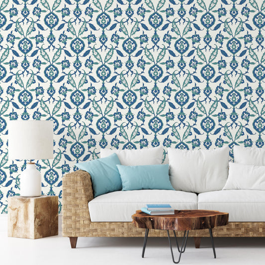 a living room with a white sofa, a wooden coffee table, and a lamp on a wooden stand. The wall behind the sofa has a blue and white floral pattern wallpaper.