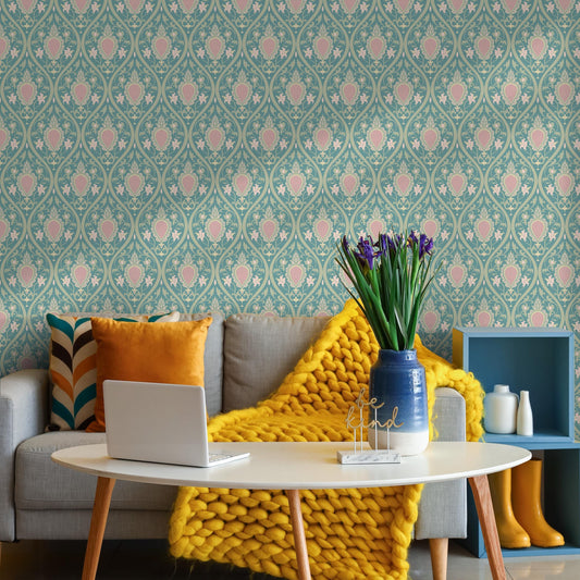 a cozy living room with a patterned wallpaper, a gray sofa with a yellow blanket, a white coffee table with a laptop and a vase of purple flowers, and a blue shelf with a white vase and a white bottle.