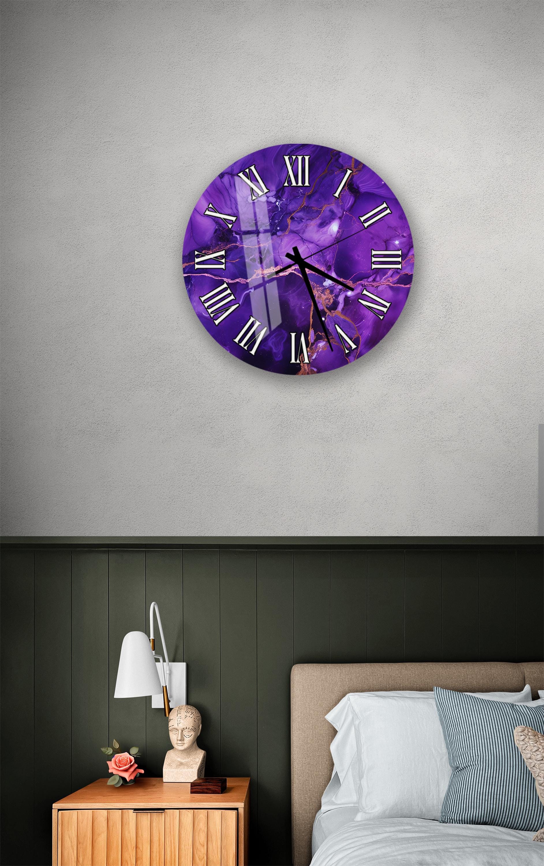 a bedroom setting with a purple wall clock hanging above a bed. The clock has a unique purple marble design and Roman numerals. The room also includes a nightstand with a lamp and a small statue or bust.