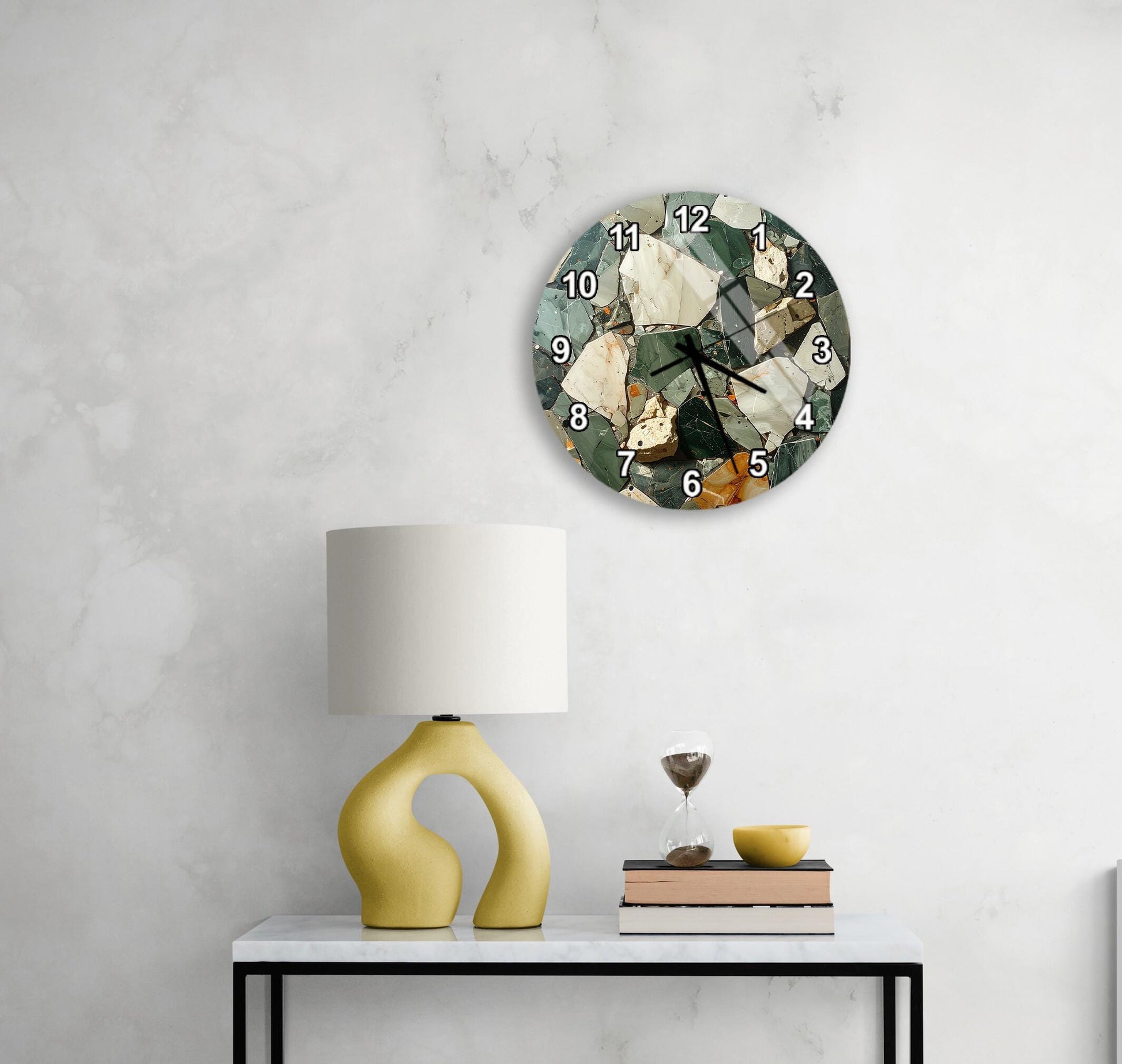 a white wall with a round clock displaying the numbers 1 through 12, a yellow lamp with a unique curved base, a stack of books, and a glass of wine on a small table.
