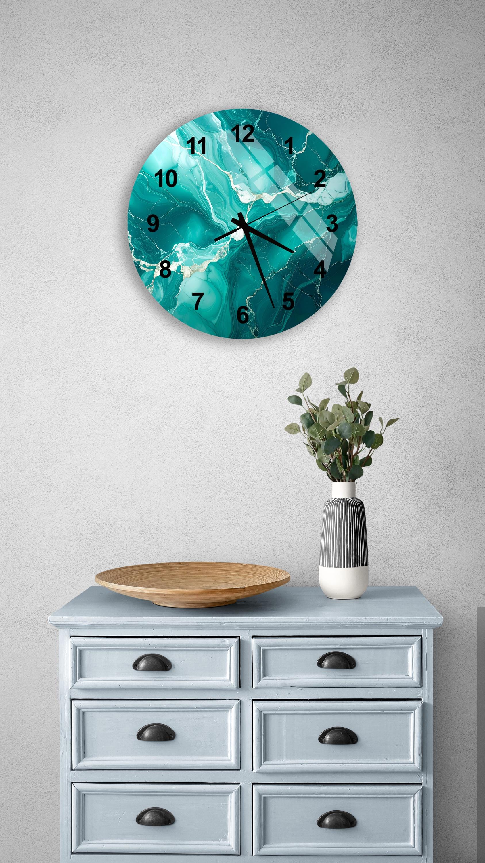 a wall clock with a turquoise marble design, mounted on a wall above a light blue dresser with six drawers. The dresser also has a vase with greenery and a wooden bowl on top.