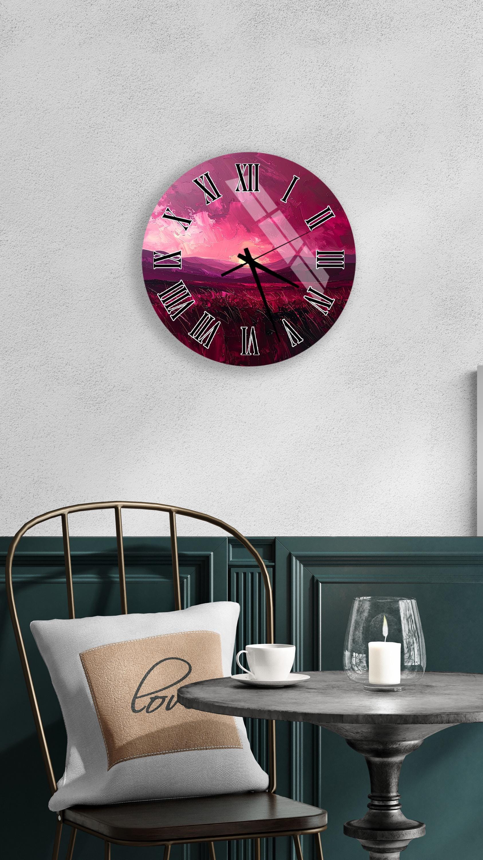 a round wall clock with a pink and purple color scheme, hanging on a white wall above a dining table with a white tablecloth. The table is set with a white cup and a candle, creating a cozy and inviting atmosphere.