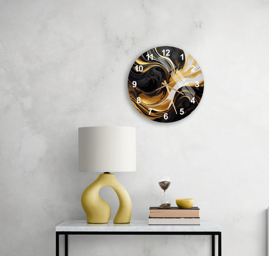 May include: A round wall clock with a black and gold abstract marble design. The clock face has white Arabic numerals. The clock hands are black. The clock is mounted on a white wall. A yellow table lamp and hourglass are on a side table below the clock.