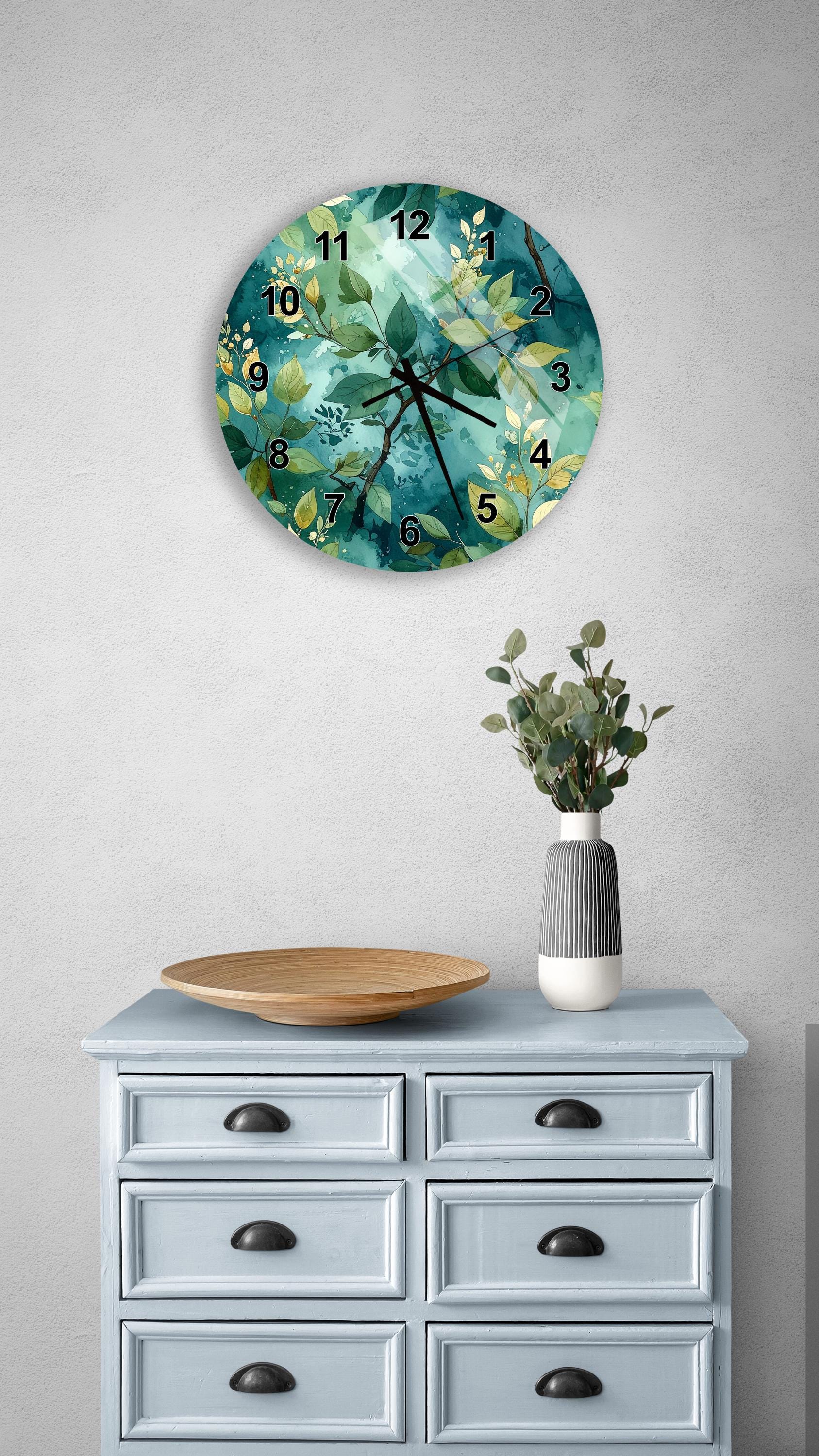 a wall clock with a green and white floral design, mounted on a wall above a light blue dresser with six drawers. The dresser also has a vase with greenery and a wooden tray on top.