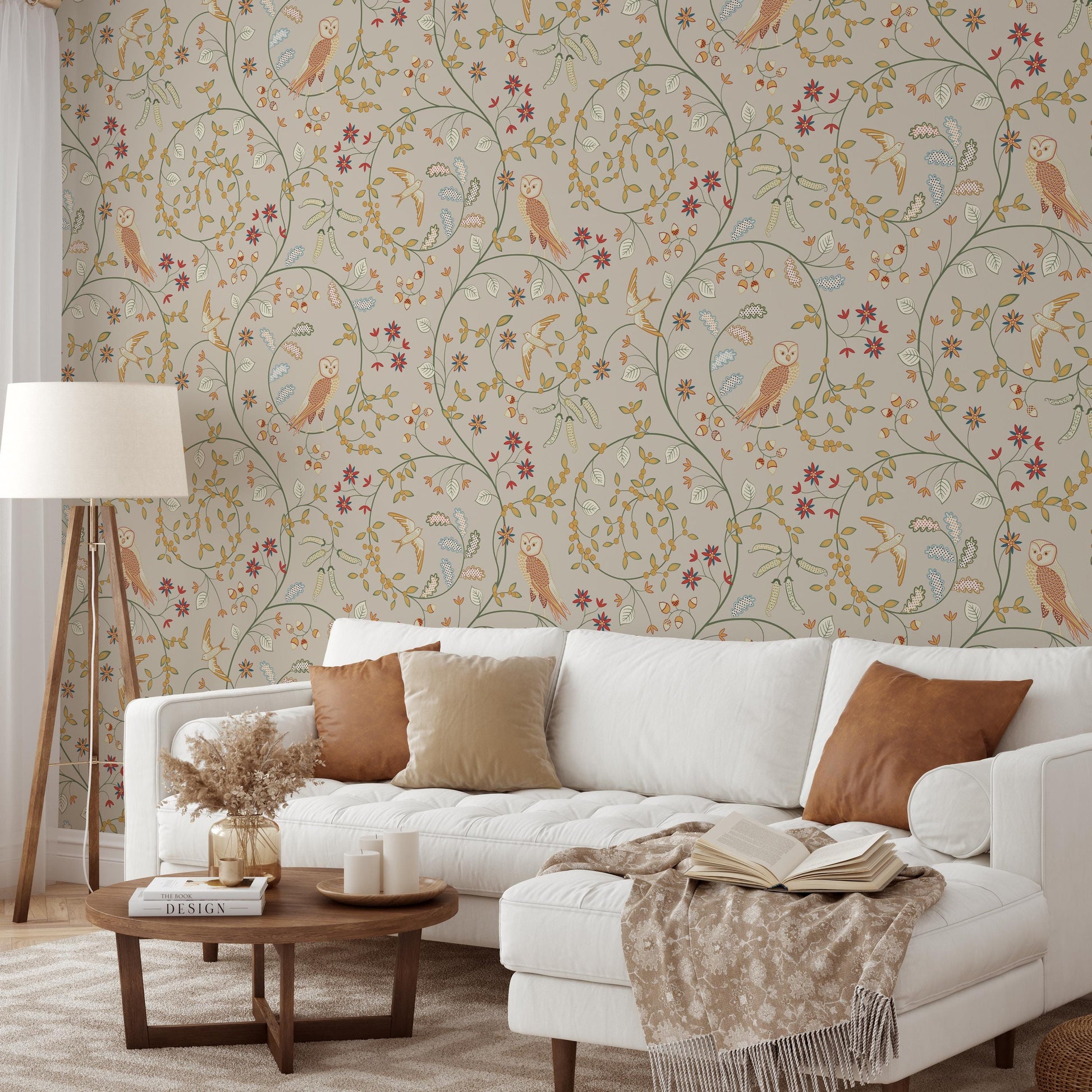 a cozy living room with a white sofa adorned with brown throw pillows, a wooden coffee table, and a lamp. The walls are decorated with a floral wallpaper pattern, and a book is placed on the coffee table.