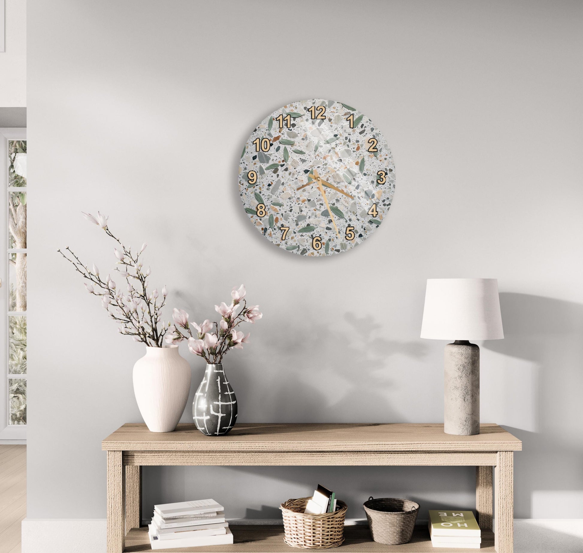 a modern and minimalist living room with a wooden console table, a round wall clock, and various decorative elements such as a vase with flowers, a lamp, and a stack of books.