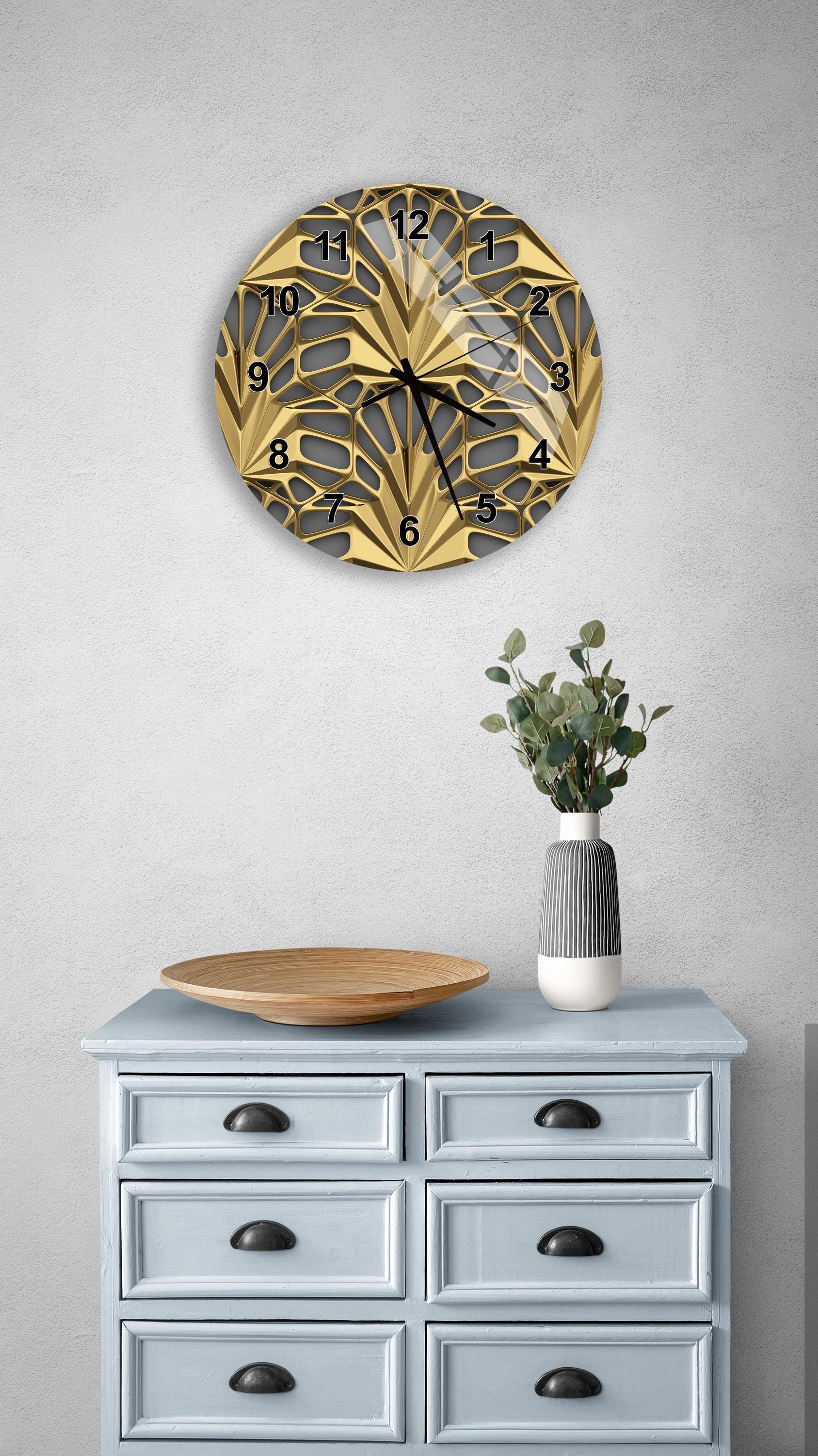 a wall clock with a gold and black design, mounted on a wall above a light blue dresser with six drawers. The dresser also has a vase with greenery on it, and a wooden bowl on top.