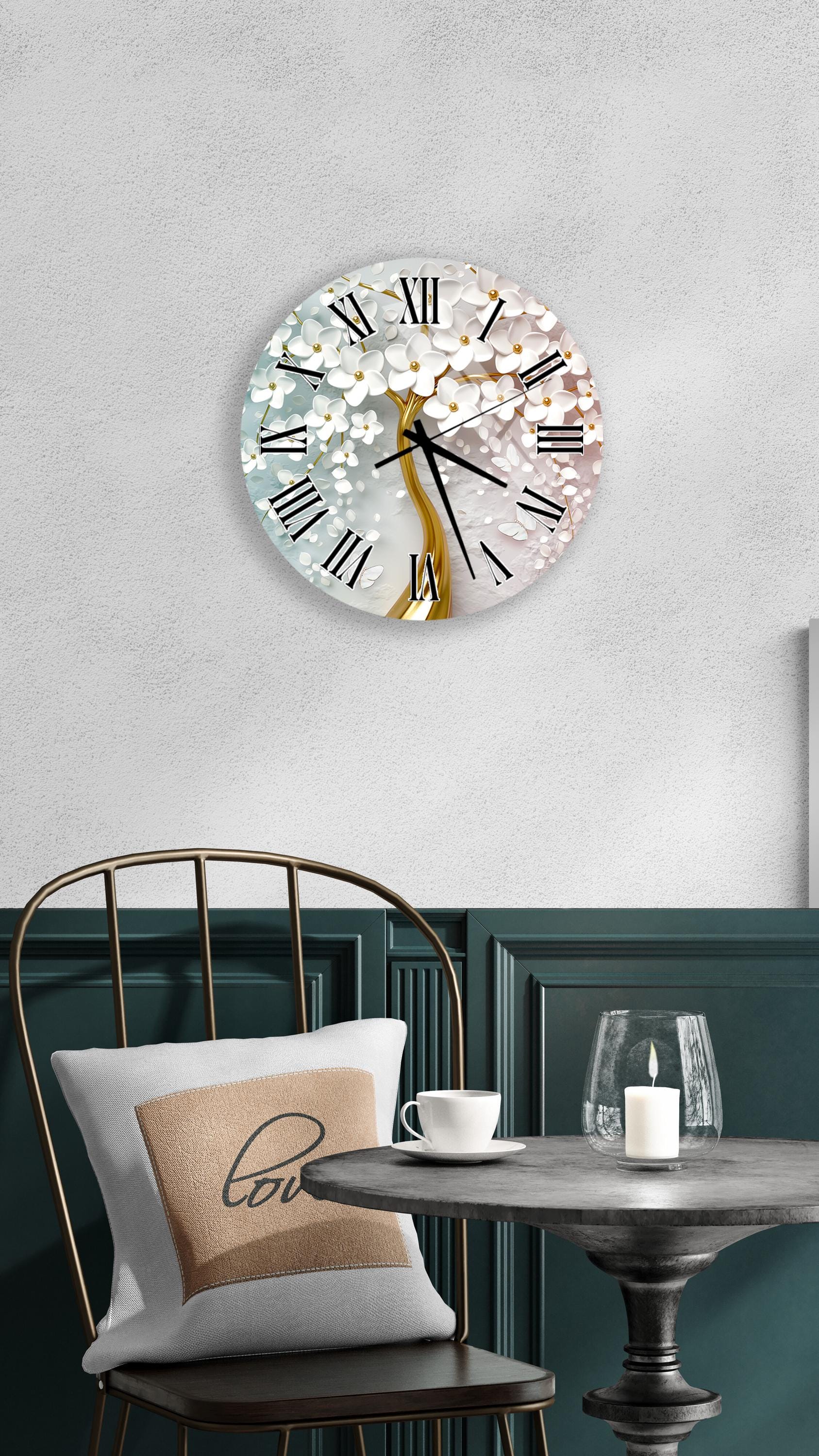 a wall clock with a white and gold design, mounted on a wall above a table with a white tablecloth. The table has a white candle and a white mug on it. A chair is positioned in front of the table, and there is a pillow with the word "love" on it.