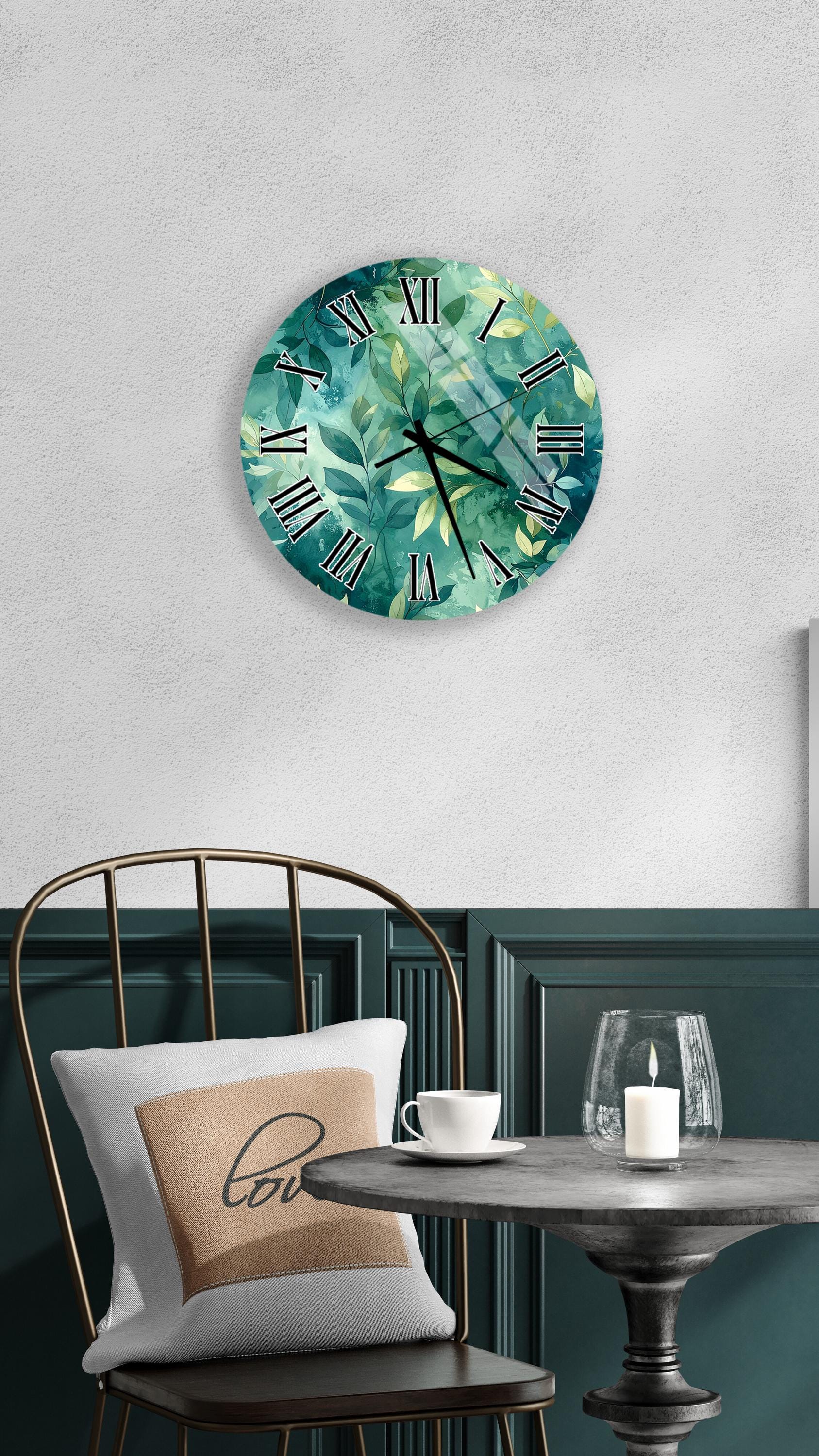 a wall clock with a green leaf design, a white table with a candle and a cup, and a black chair with a pillow.