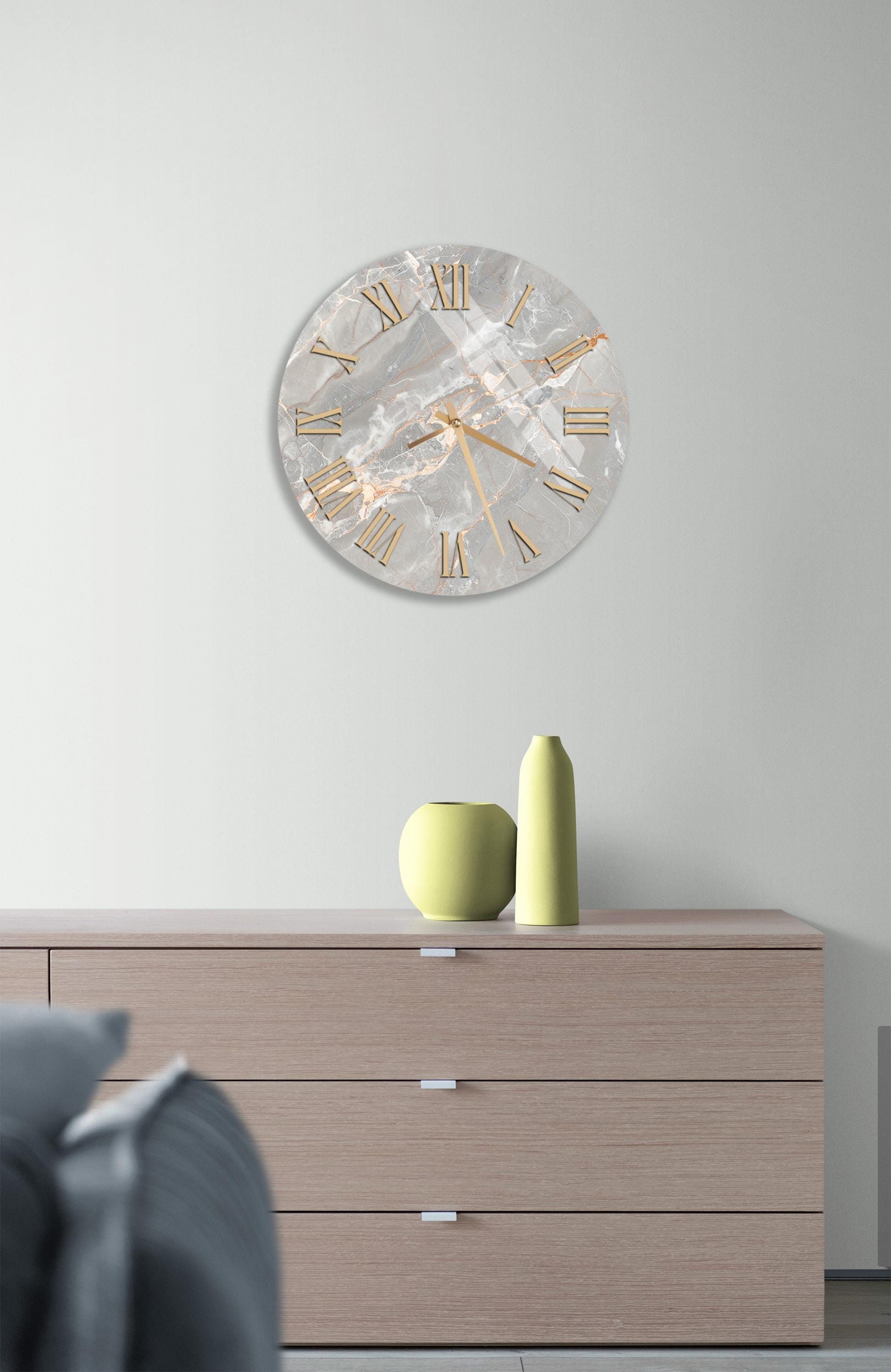 a modern living room with a large, round clock hanging on the wall above a wooden dresser. The clock has a marble-like finish and gold Roman numerals. On the dresser, there are two yellow vases and a small green vase, creating a stylish and cohesive decor.