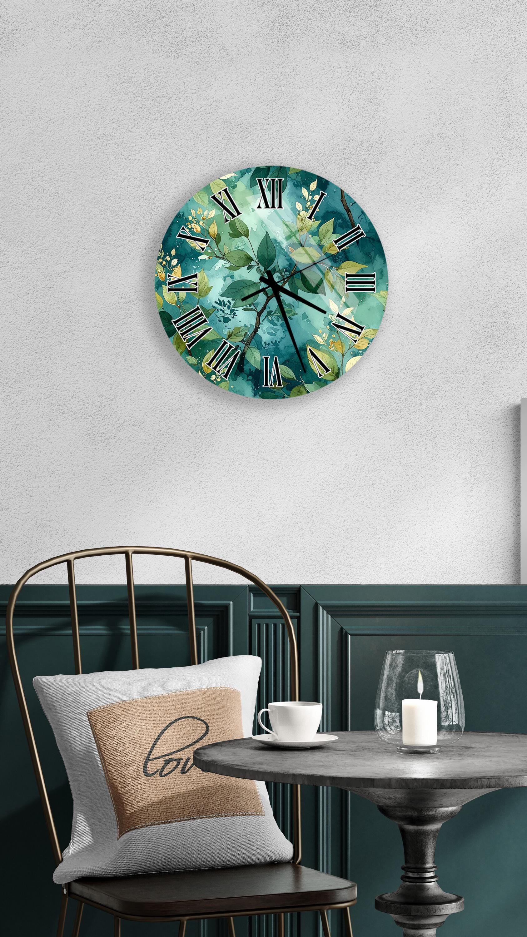 a round wall clock with a green and white floral design, mounted on a white wall above a black metal chair. The chair has a white pillow with the word "love" printed on it. In front of the chair, there is a small table with a glass candle holder and a white teacup.