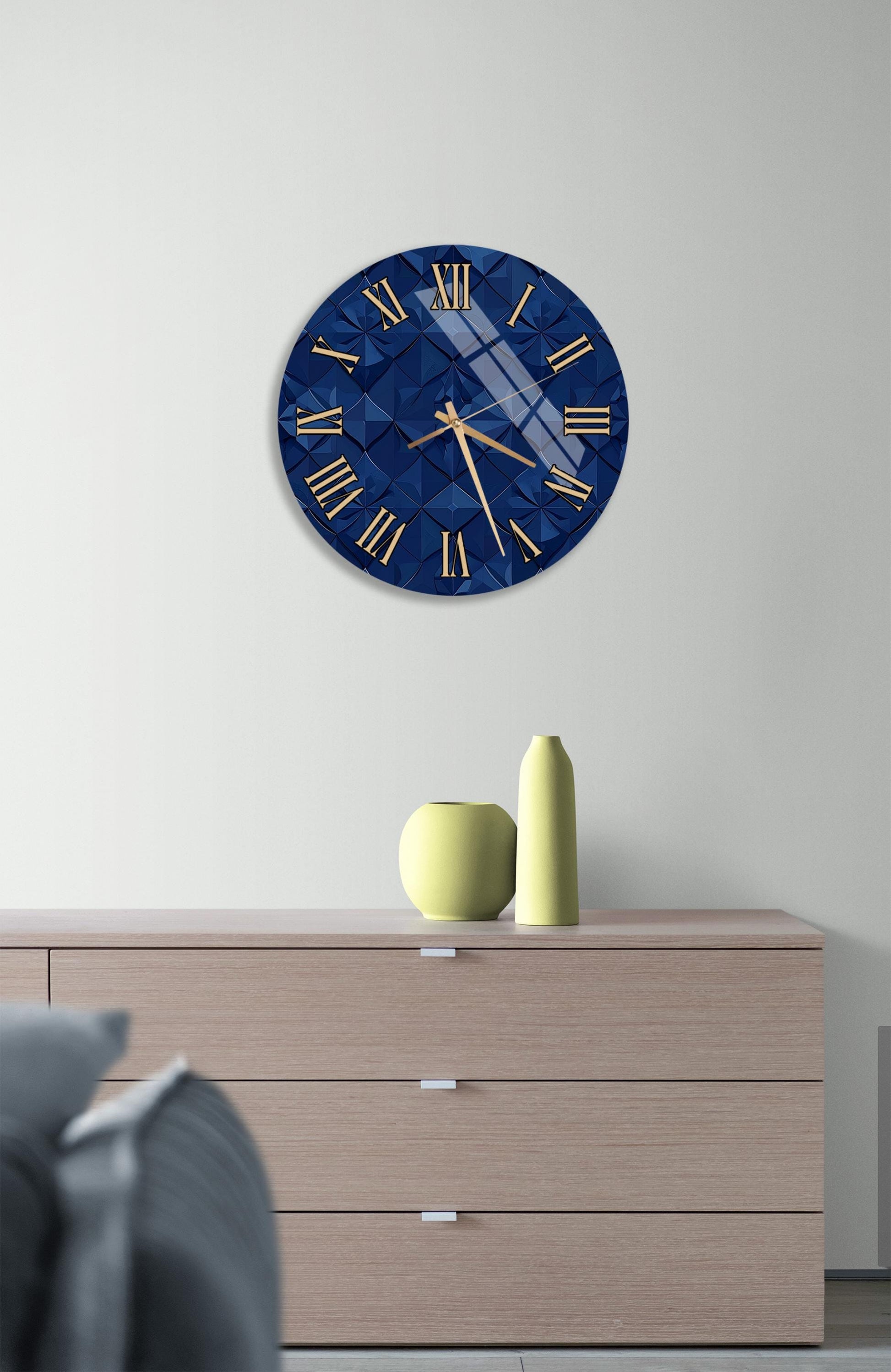 a modern interior design with a blue and gold clock on a white wall above a wooden dresser. The dresser has three drawers and a vase on top.