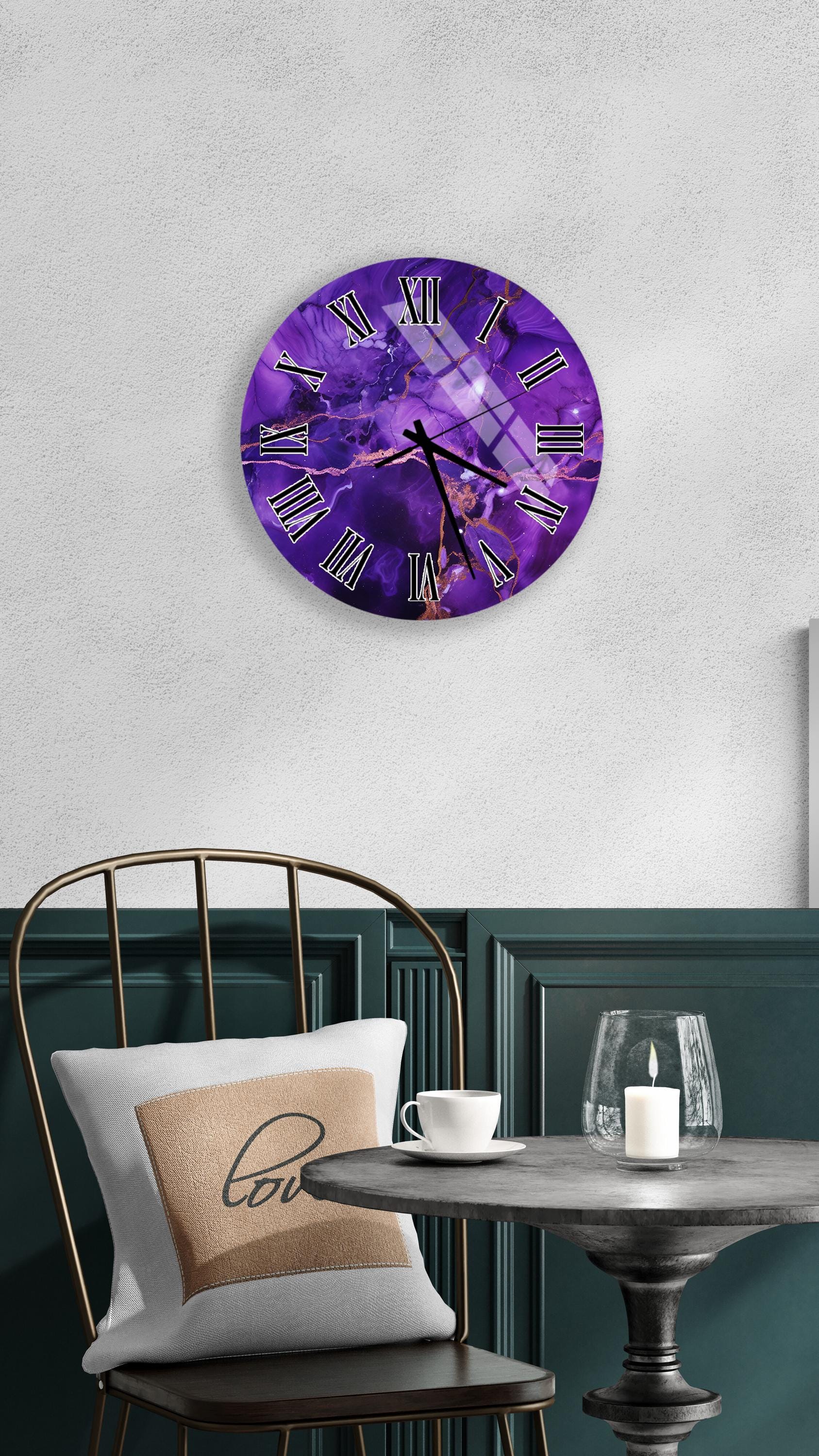 a purple wall clock with a purple and white design, mounted on a white wall above a dining table with a white tablecloth. The table has a white cup and a candle on it, creating a cozy and inviting atmosphere.