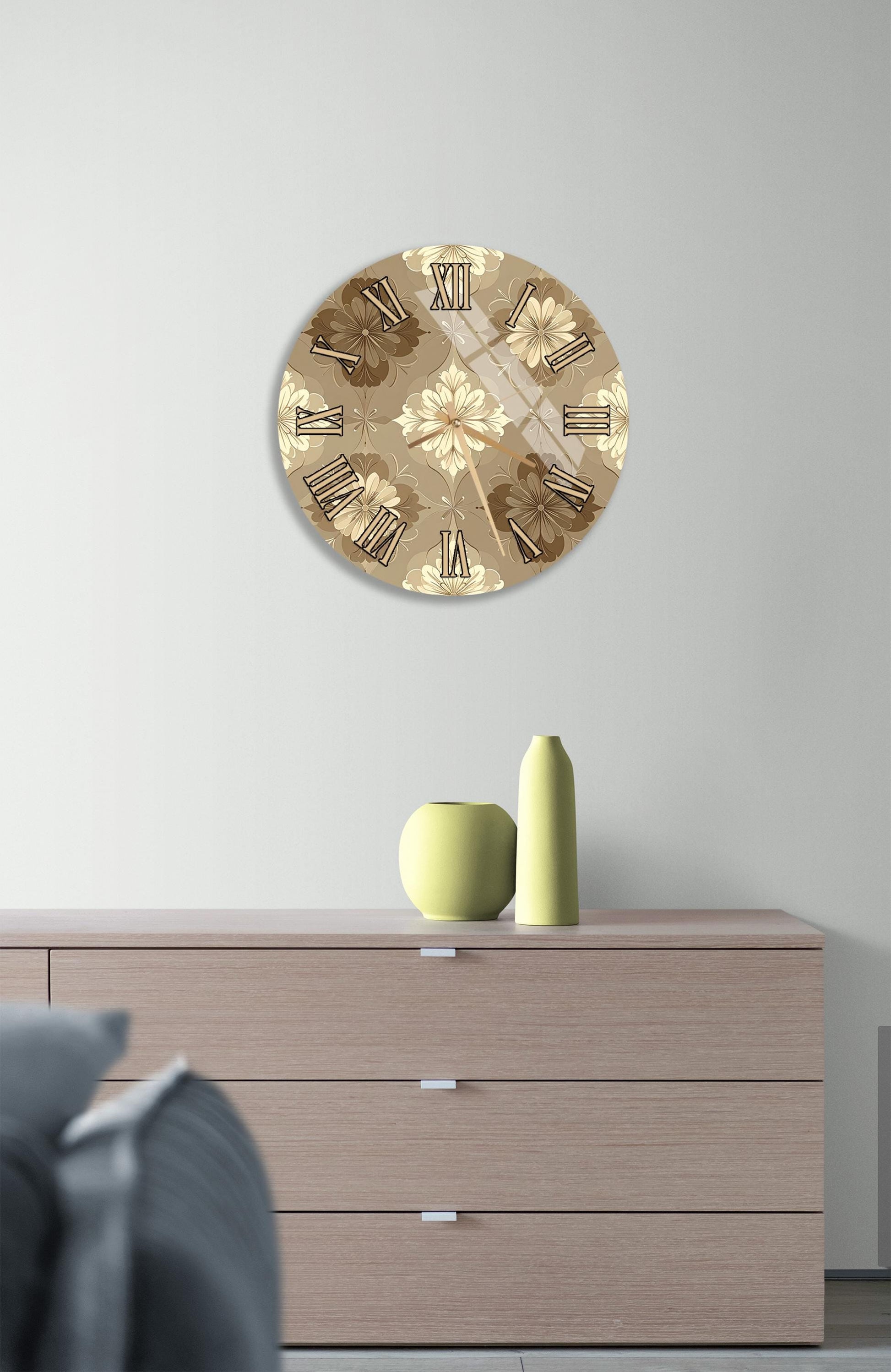a round clock with a floral design on a white wall, hanging above a wooden dresser with a green vase and a yellow pot on top.