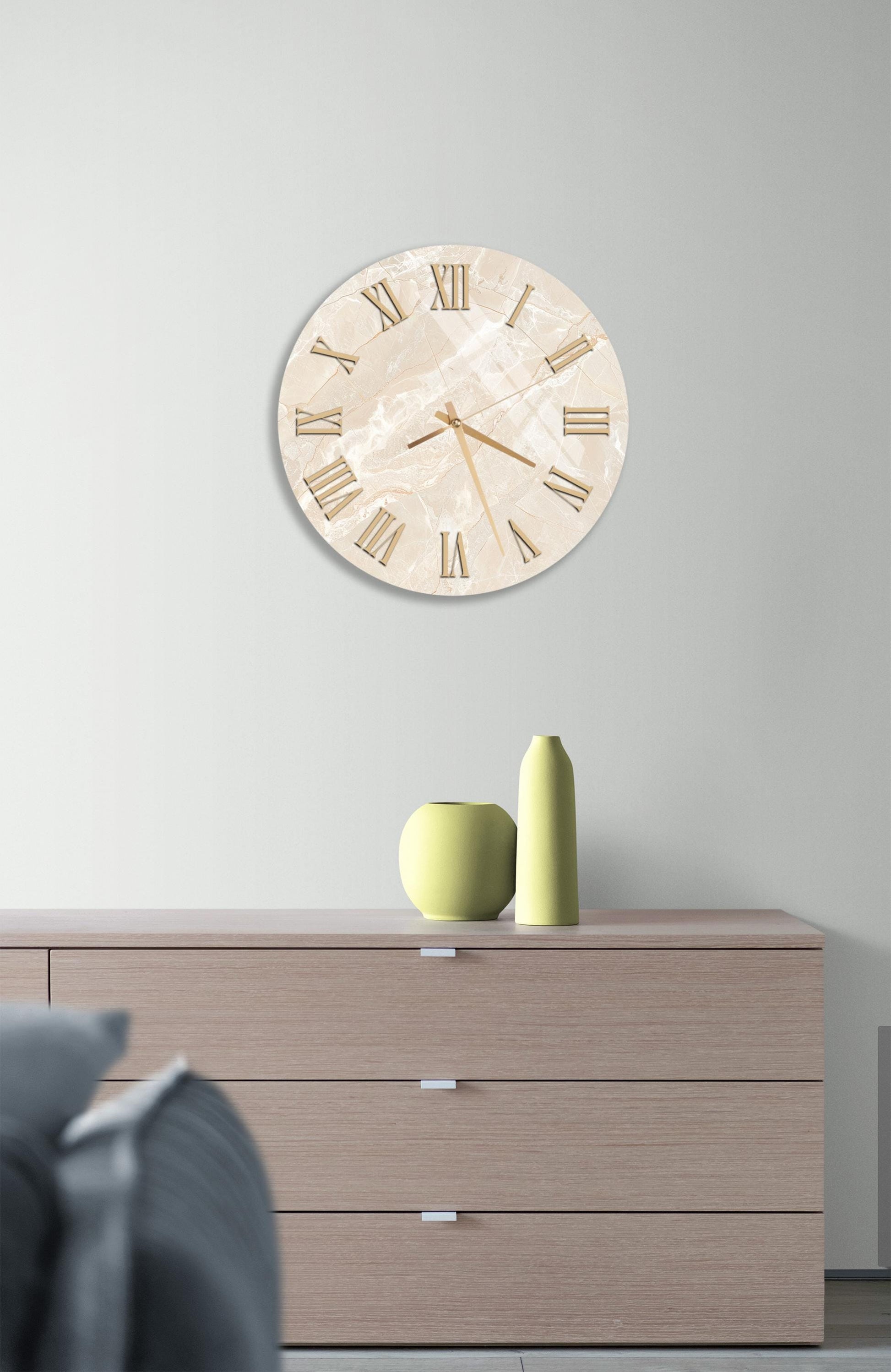 a modern living room with a large round clock on the wall above a wooden dresser. The clock has a marble-like finish and Roman numerals. On the dresser, there are two yellow vases and a green vase, creating a stylish and cohesive decor.