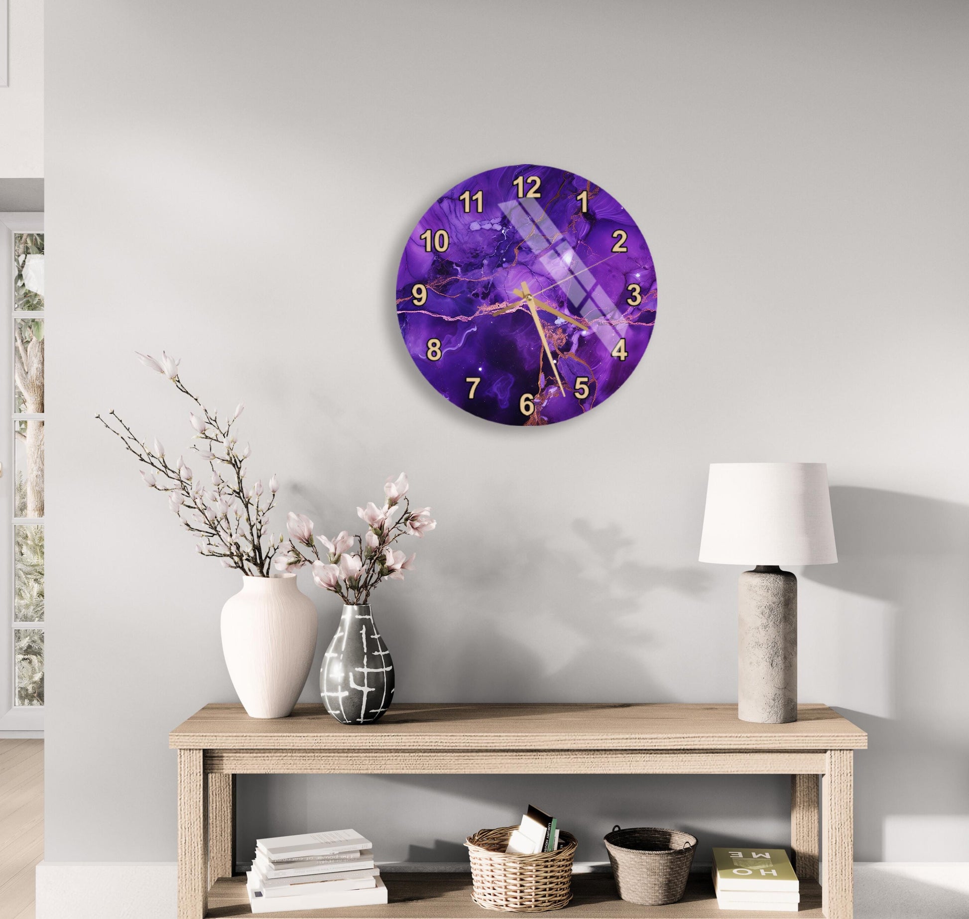 a modern living room with a wooden table, a lamp, a clock, and a vase with flowers. The clock has a purple and gold design, and the table has a white vase with pink flowers. The lamp is positioned next to the table, and the wall behind the table has a clock hanging on it.