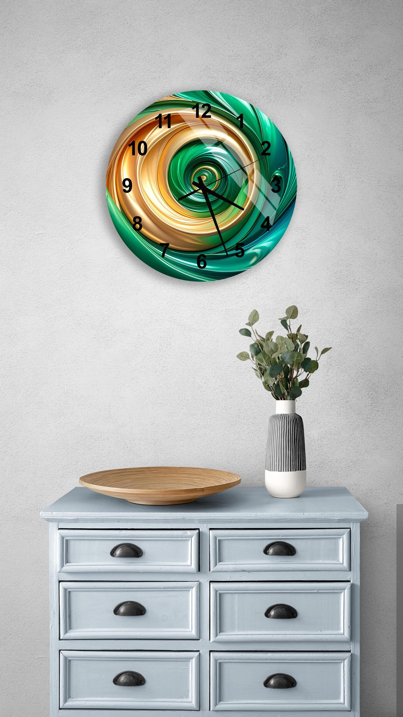 a wall clock with a spiral design in green, orange, and yellow colors, mounted on a gray wall above a light blue dresser with six drawers. The dresser also has a vase with greenery and a wooden tray on top.