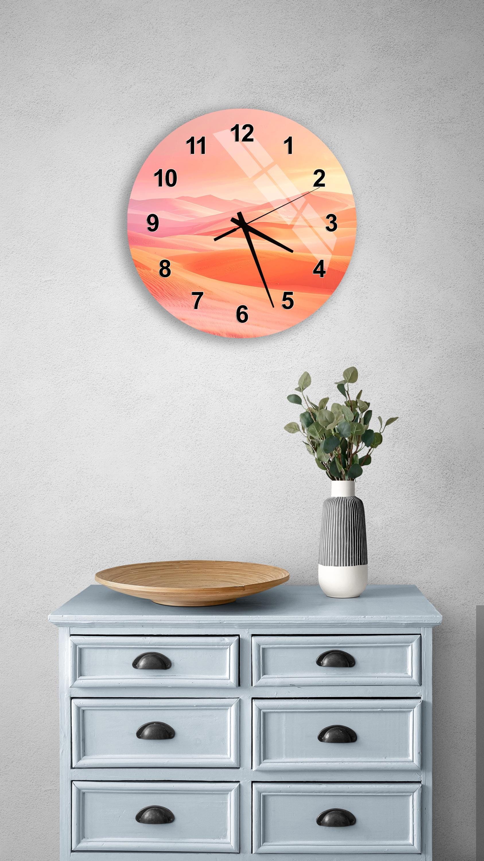 a wall clock with a sunset-themed design, mounted on a wall above a wooden dresser with drawers. The dresser also has a vase with greenery and a wooden tray on top.