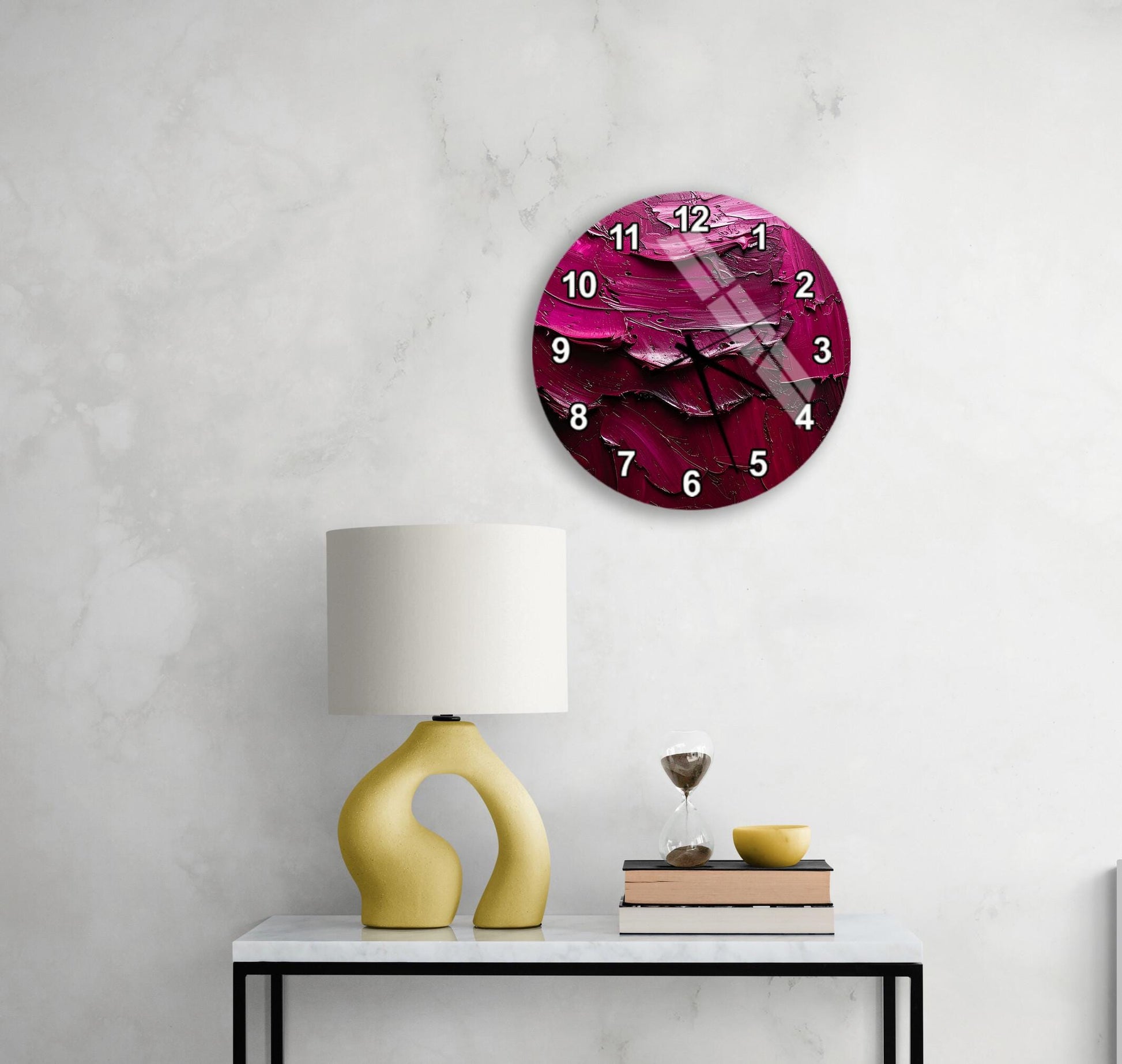 a modern, minimalist living space with a white marble wall, a round clock with a pink and purple abstract design, a yellow lamp with a unique, curved base, and a small table with a book and a glass of water.
