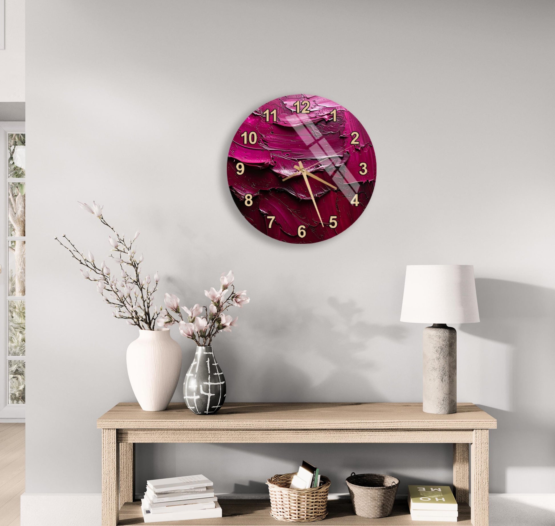 a modern living room with a round wall clock displaying a pink and purple abstract design, a wooden table with a lamp, a vase with pink flowers, and a stack of books.