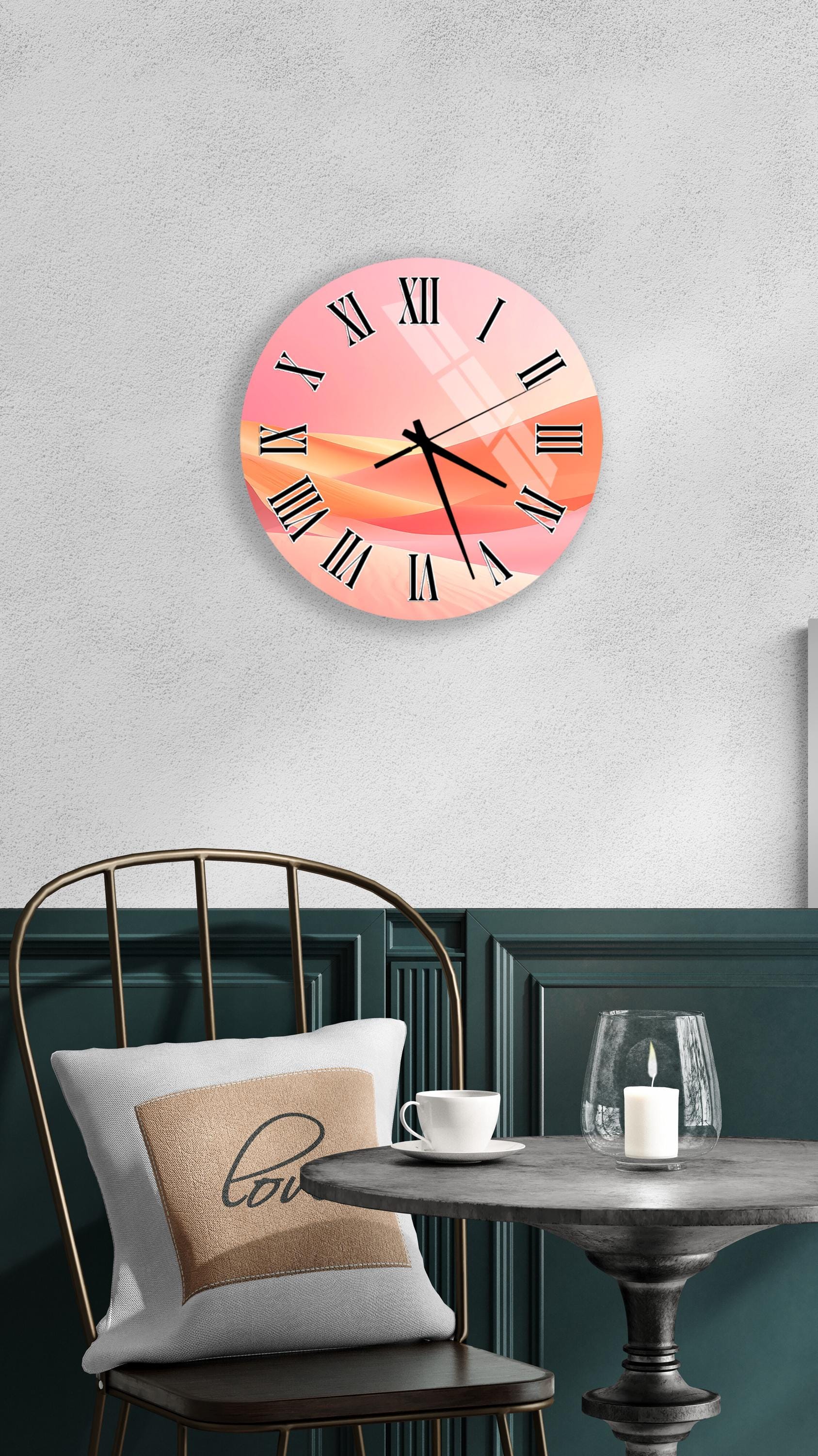 a wall clock with a pink and orange abstract design, mounted on a wall above a table with a white tablecloth. The table has a glass candle and a white coffee cup on it.