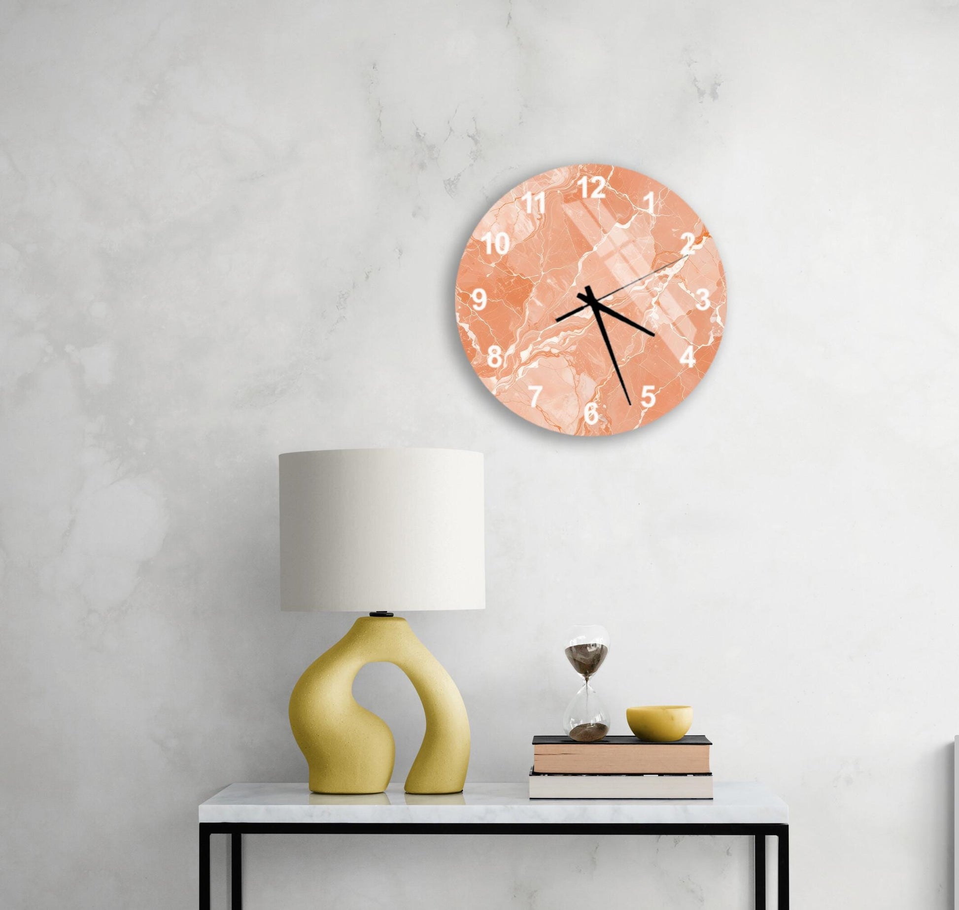 a modern living room with a white marble wall, a round orange clock with a marble pattern, a yellow lamp with a unique curved base, a stack of books, and a glass of wine on a white table.