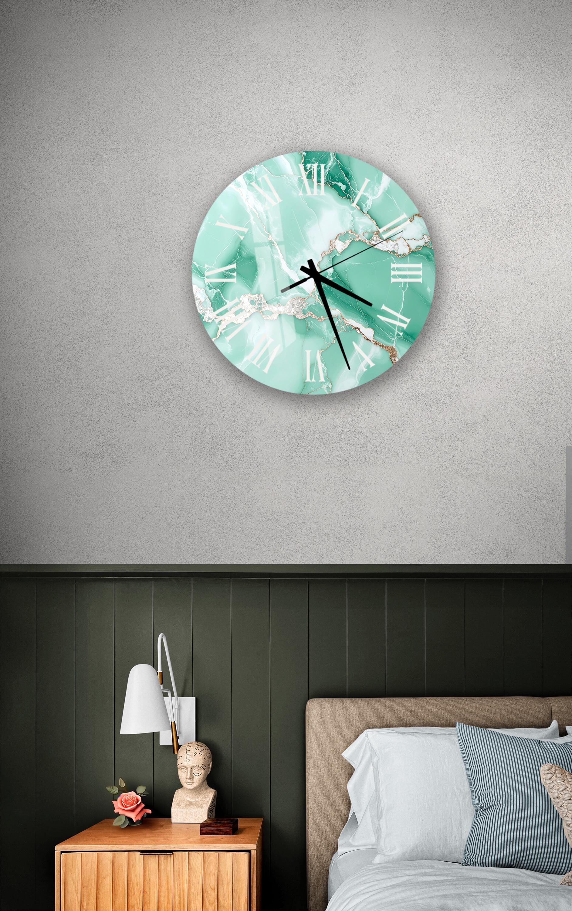 a bedroom setting with a large wall clock displaying a turquoise color scheme. The clock is mounted on the wall above a bed with a white headboard. The room also includes a nightstand with a lamp and a small statue or bust.