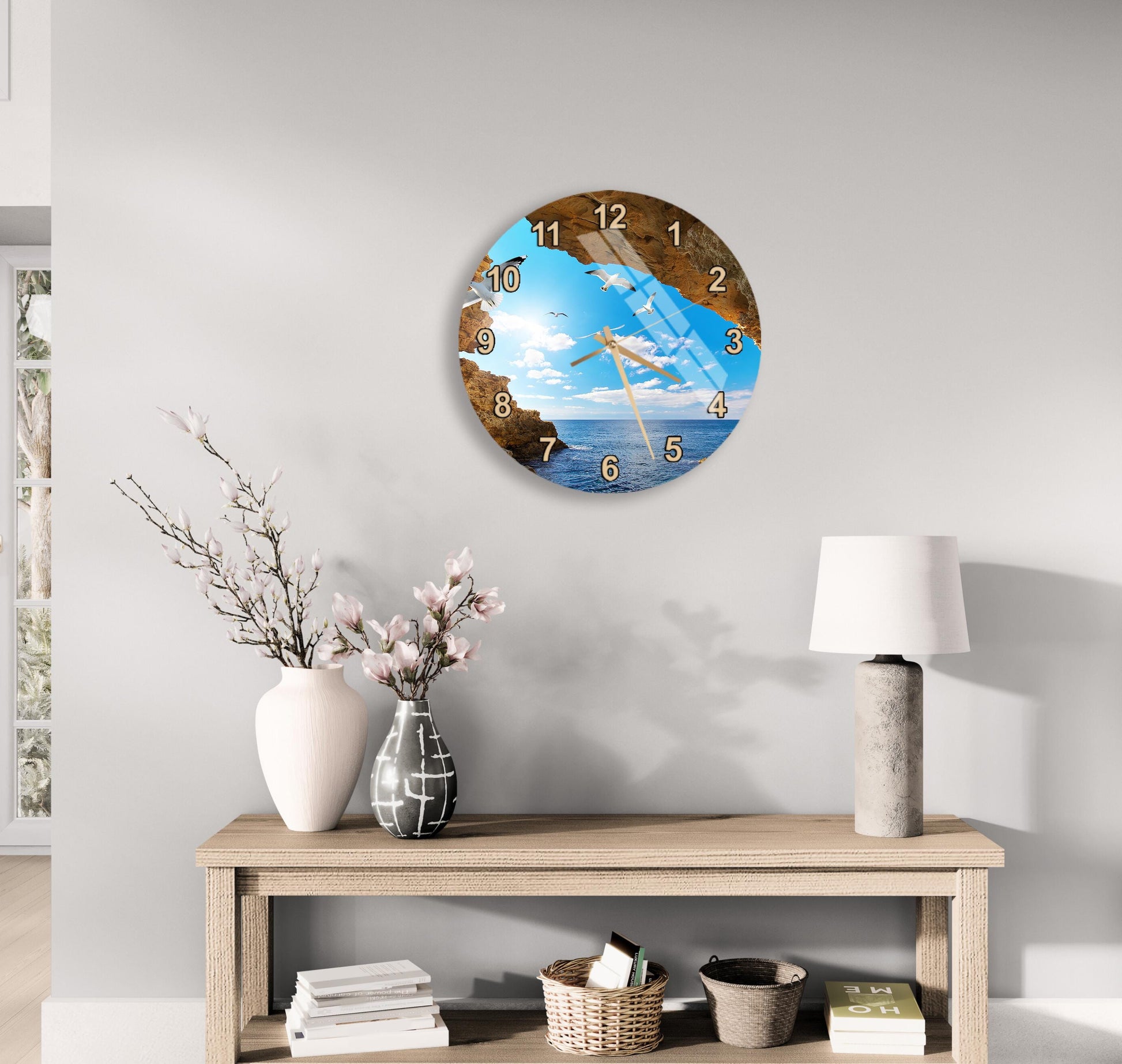 a wall clock with a beach scene, a wooden table with a vase of flowers, a lamp, and some books on a shelf.