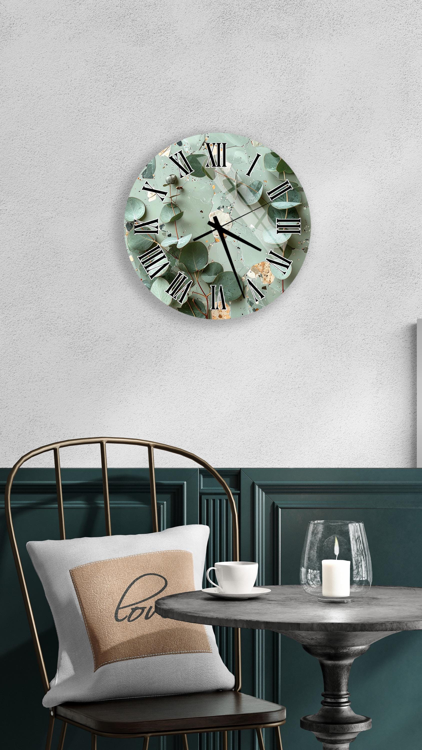 a wall clock with a green and gold design, a white table with a candle and a cup, and a black chair with a pillow.