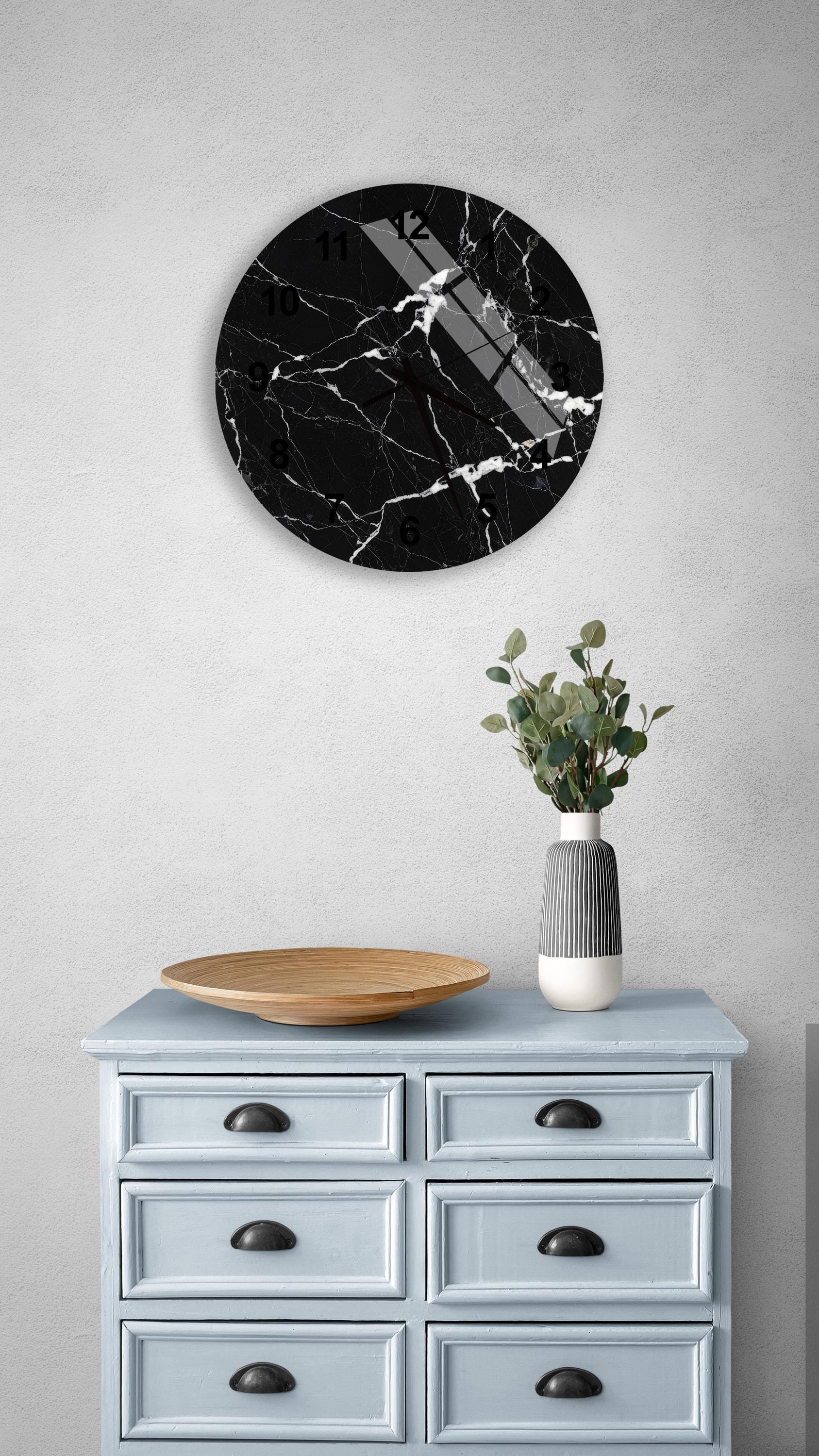 a black and white marble clock mounted on a white wall above a light blue wooden dresser with six drawers. The dresser also has a wooden bowl and a vase with greenery on it.
