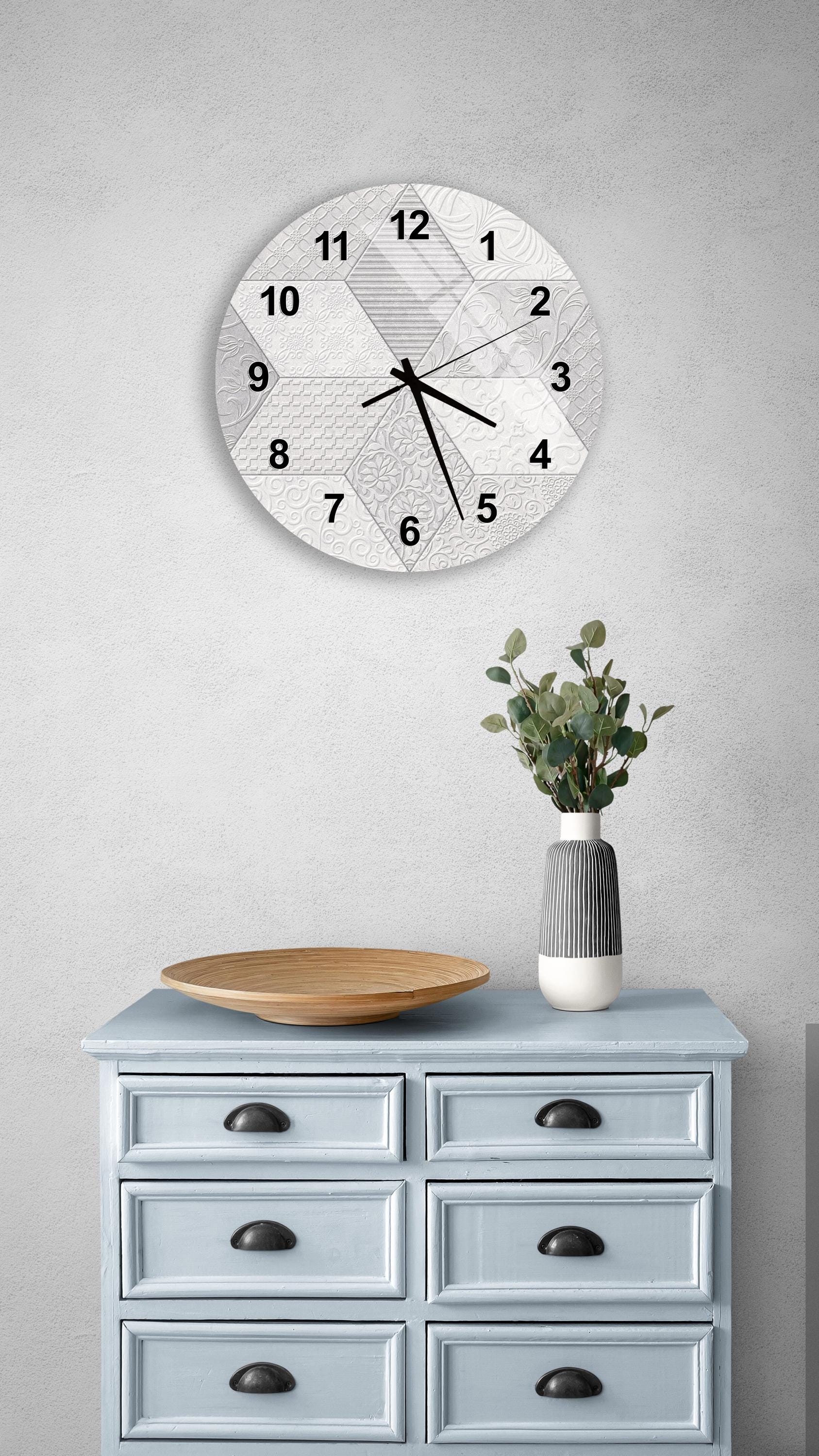 a wall clock with a geometric pattern, a wooden bowl on a light blue dresser, and a vase with greenery.