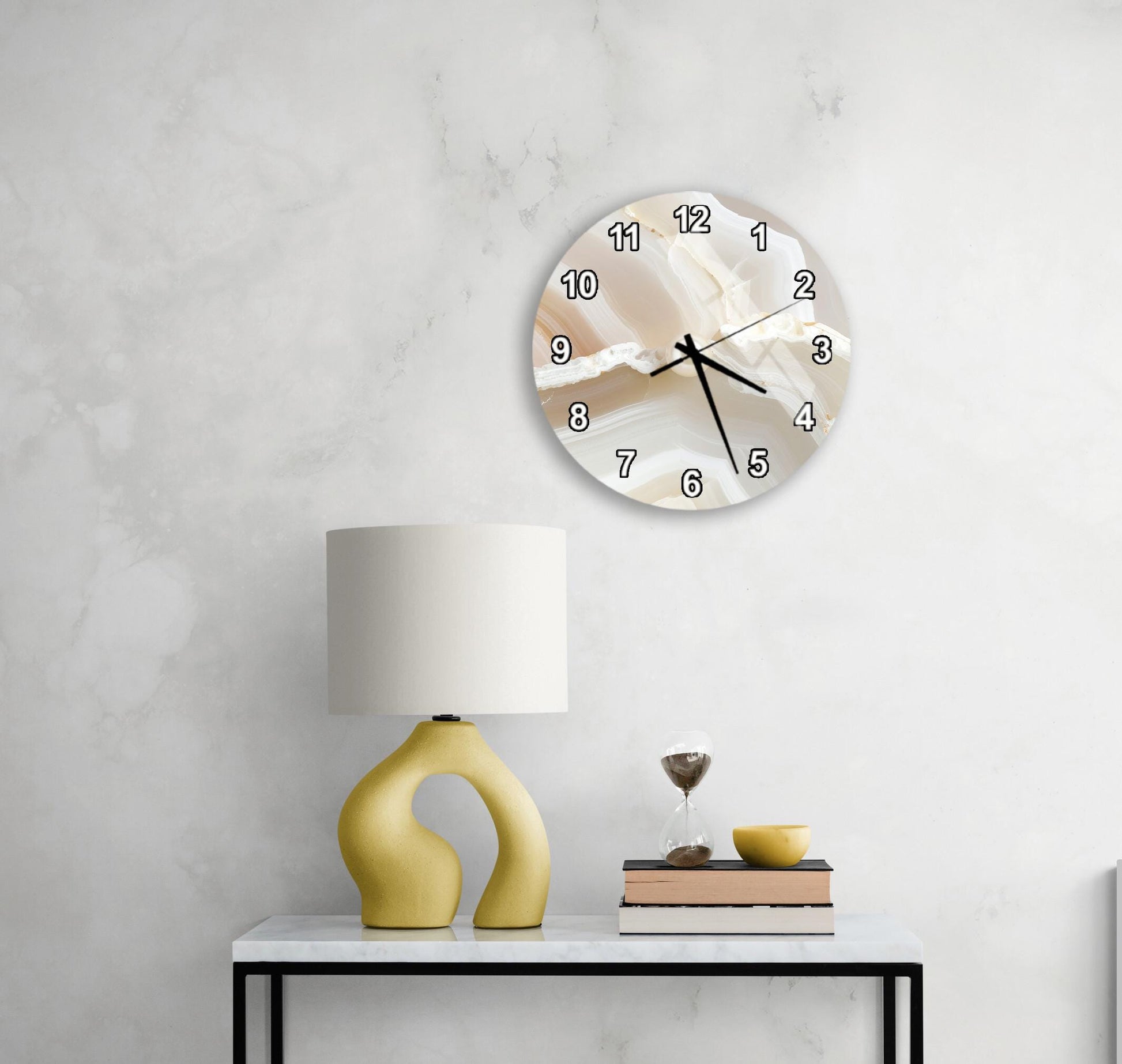a modern living room with a white marble wall, a round clock with a white face and black numbers, a yellow lamp with a unique curved base, and a small table with a stack of books and a glass of wine.