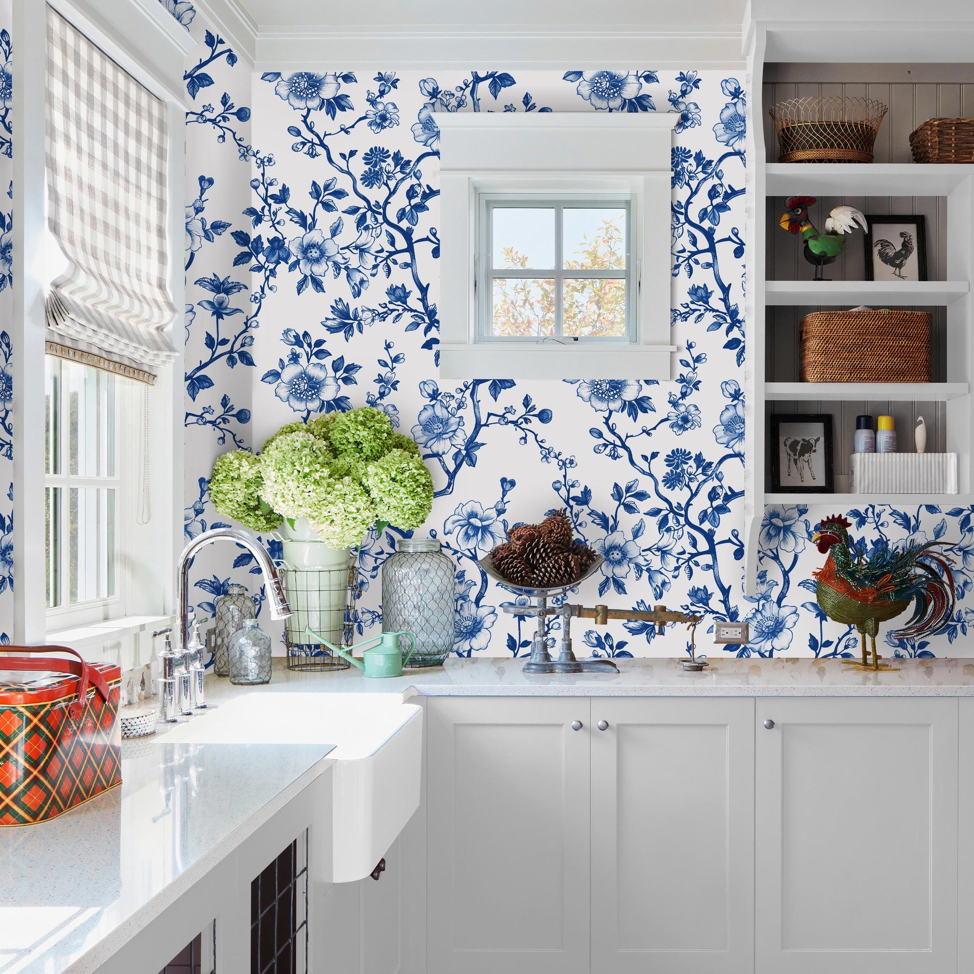 a well-decorated kitchen with a white color scheme and blue floral wallpaper. The kitchen features a sink, cabinets, and a window with a white frame. The countertop is adorned with various decorative items, including a vase, a potted plant, and a basket. The overall scene conveys a sense of cleanliness and organization, with the blue and white color palette creating a harmonious and visually appealing atmosphere.